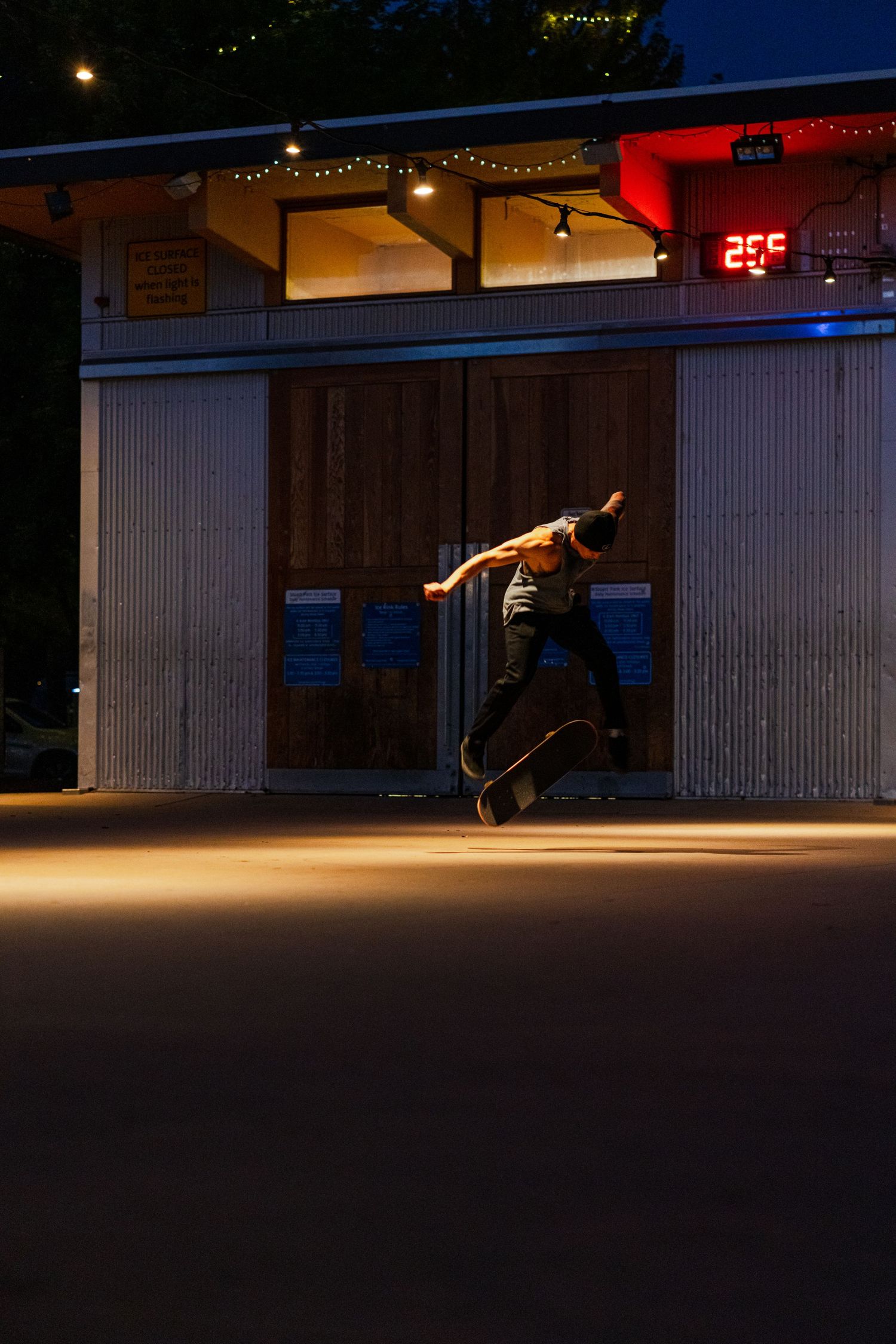 Silhouetted skateboarder performing trick in dark urban setting with illuminated building.