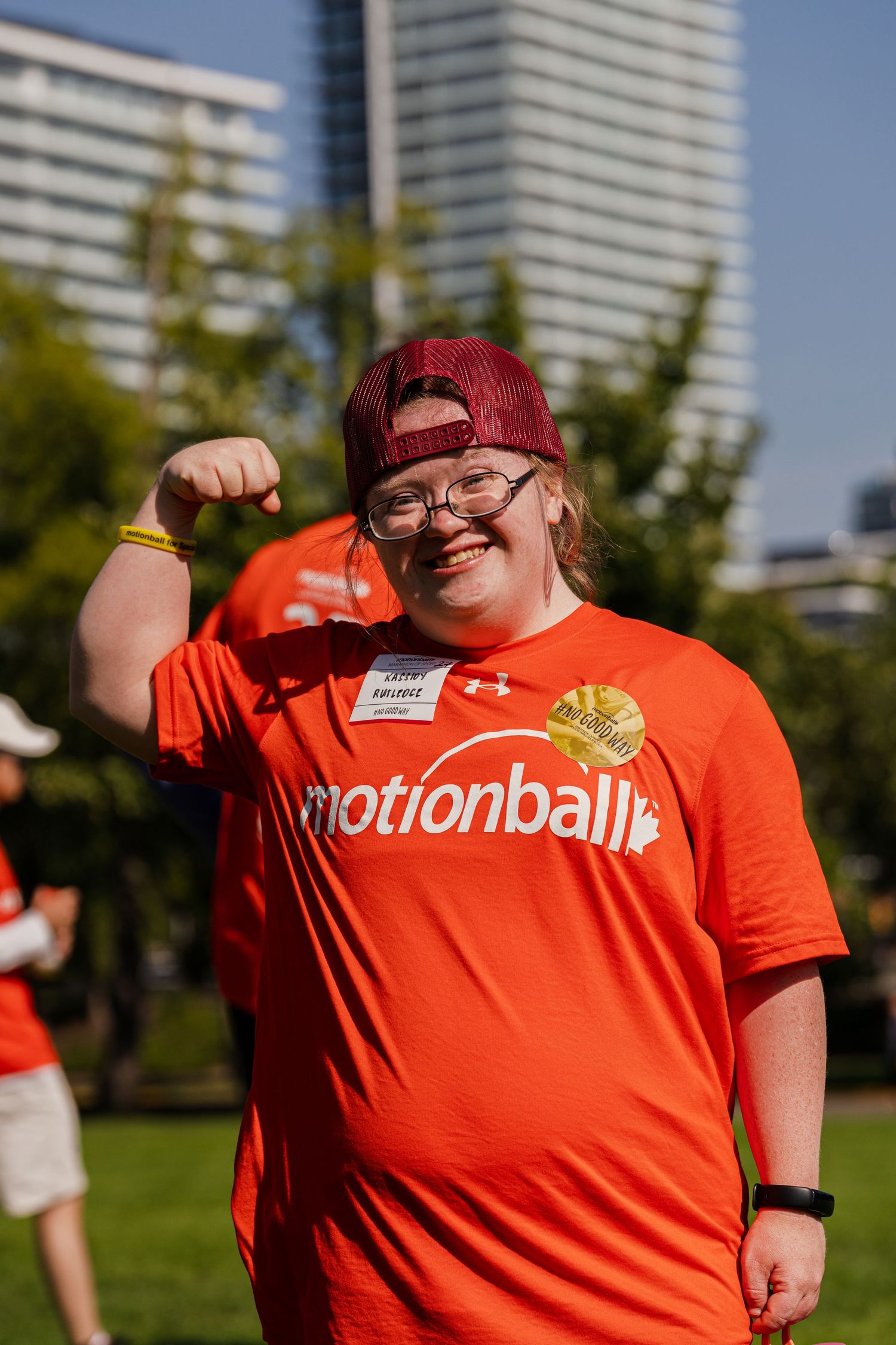 Athletes in bright orange jerseys gather outdoors on a sunny day with city buildings in the background.