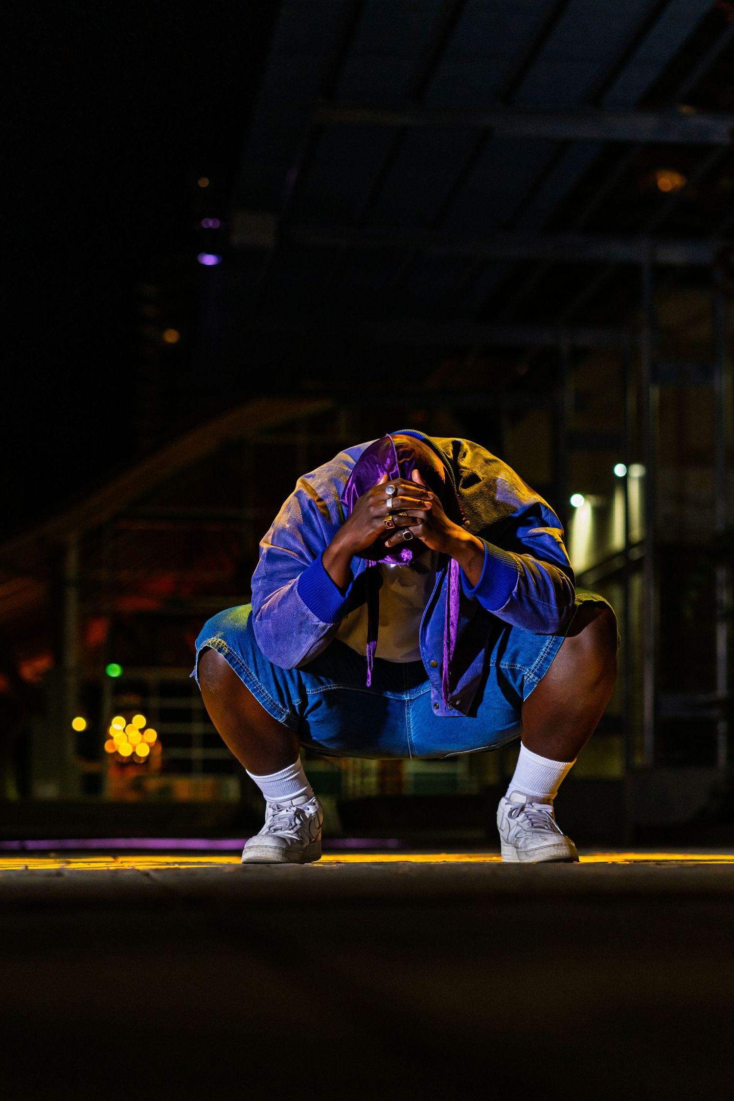 Person in blue athletic wear crouches under dramatic lighting on a dark stage with yellow spotlights.