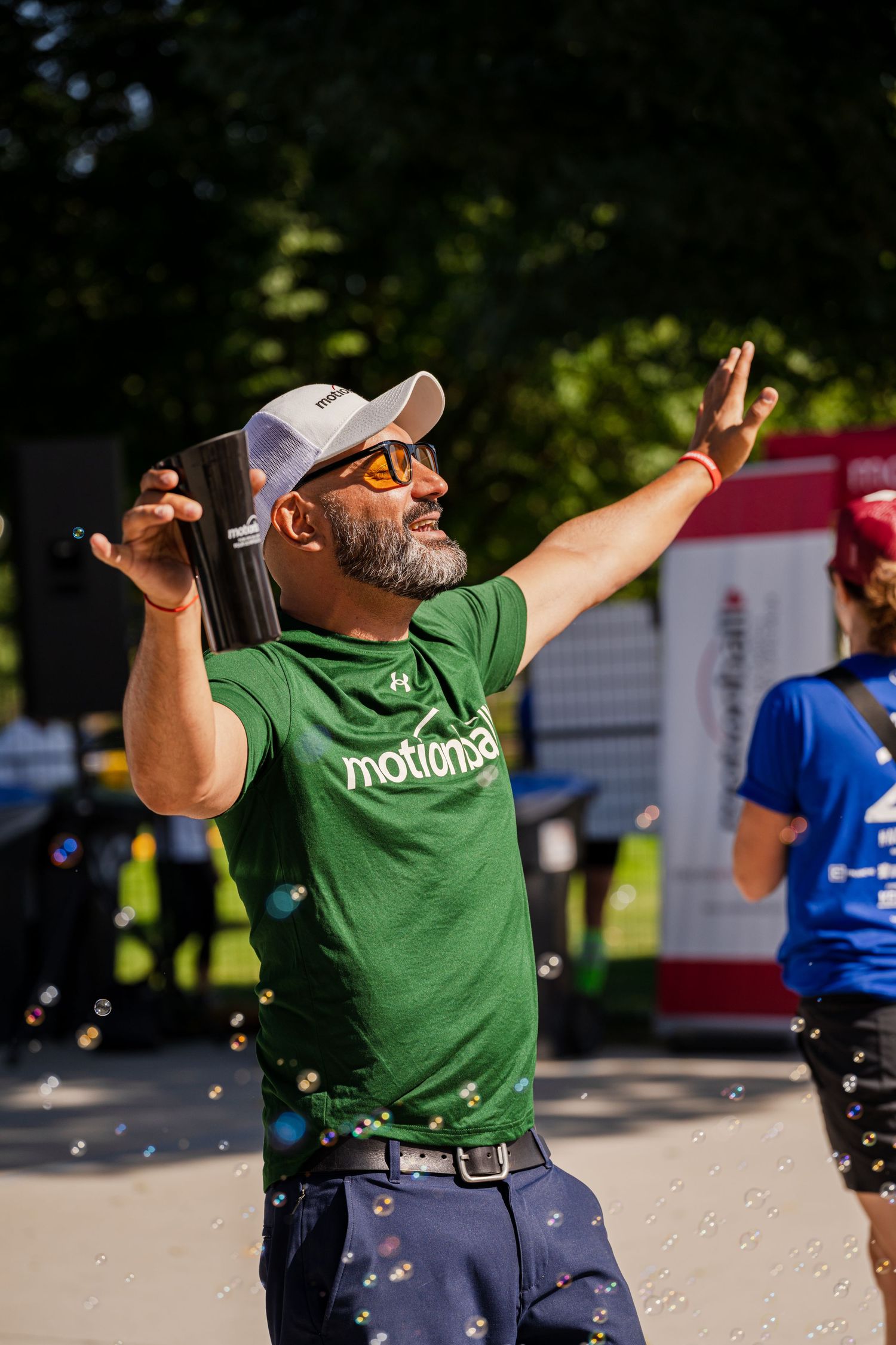 Person in green t-shirt performs an animated dance move outdoors during a daytime event.