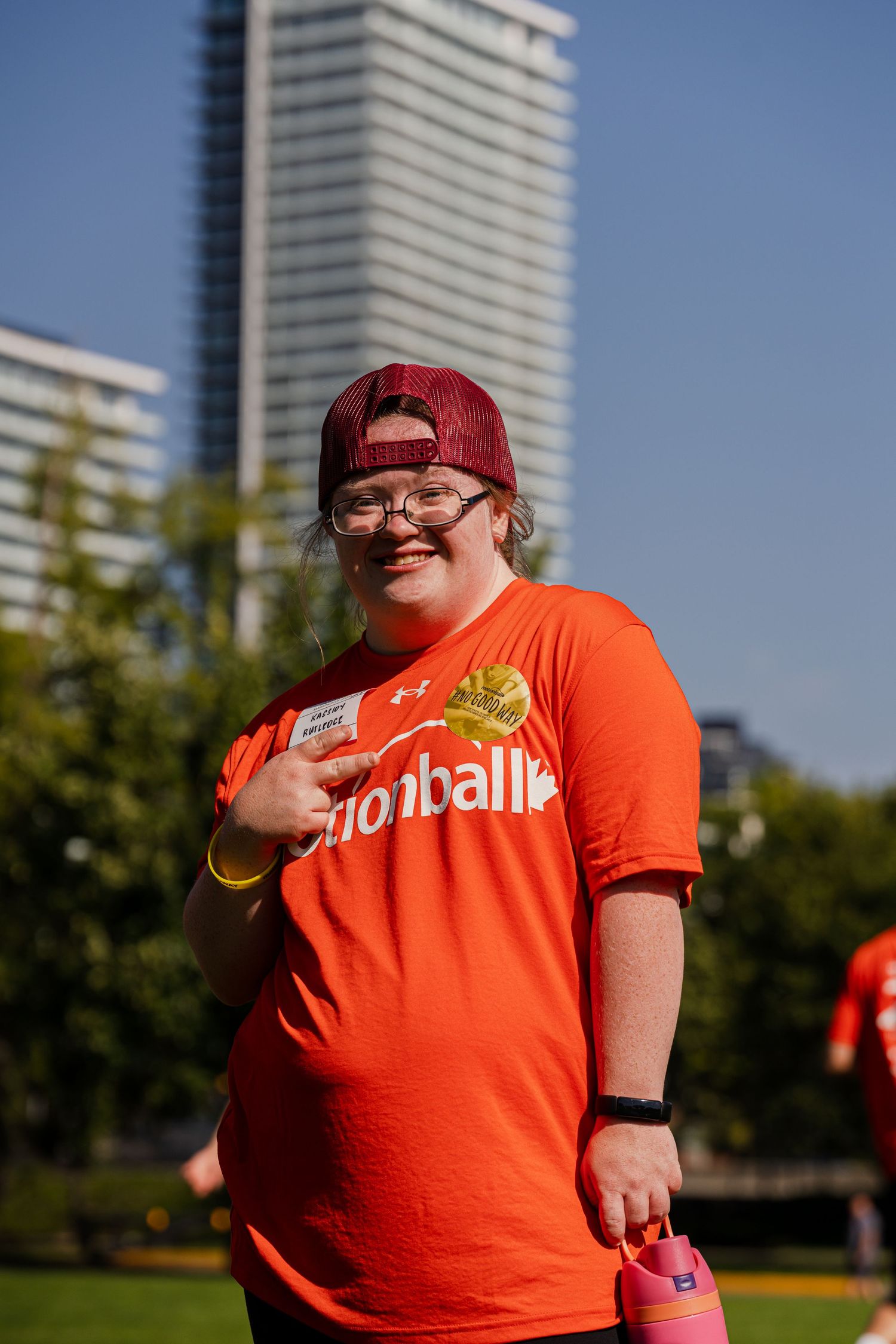 Person in bright orange t-shirt standing in front of urban high-rise building.