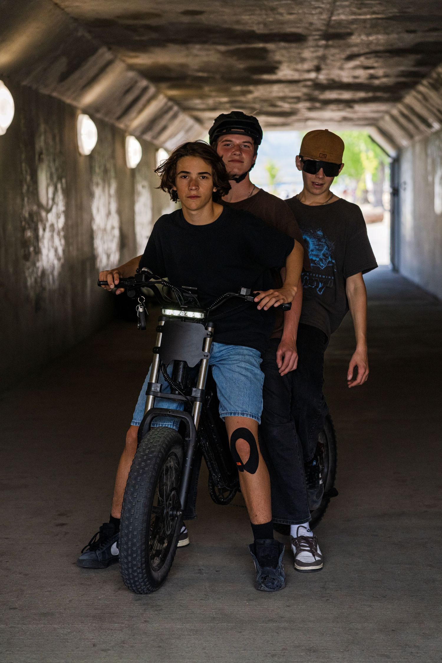 Three young people with bikes posing together in a concrete tunnel.