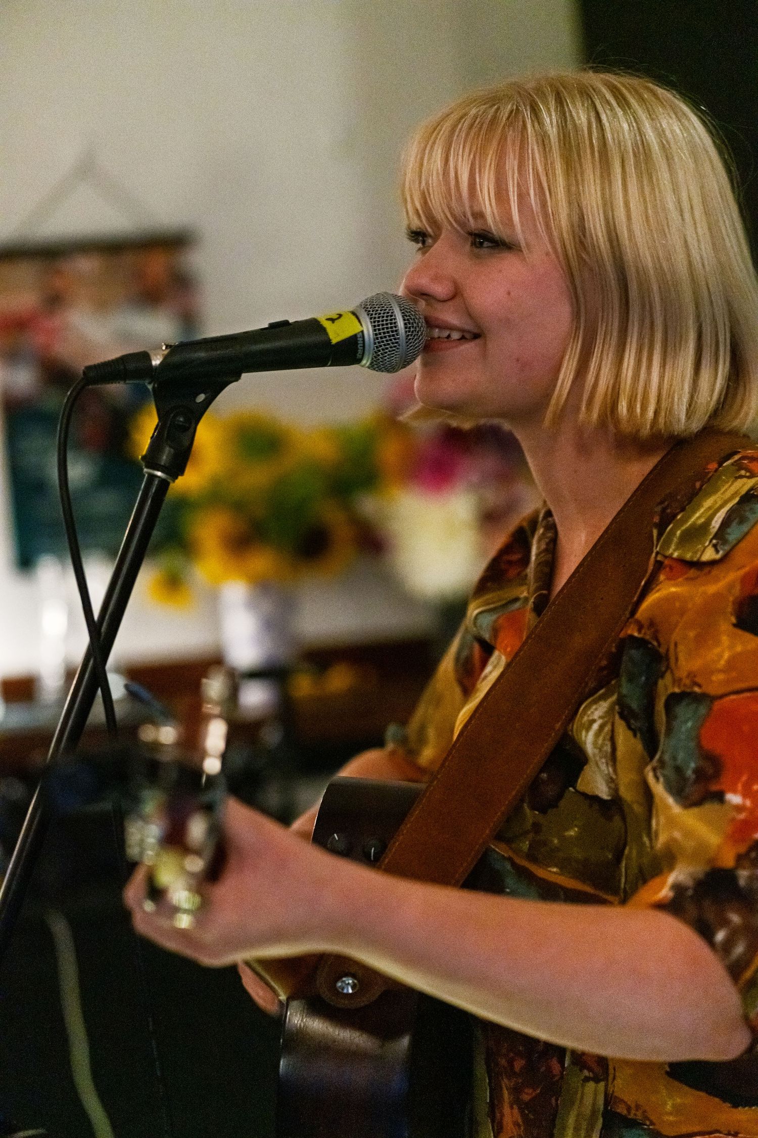 Musician in floral print shirt performing with acoustic guitar and microphone.