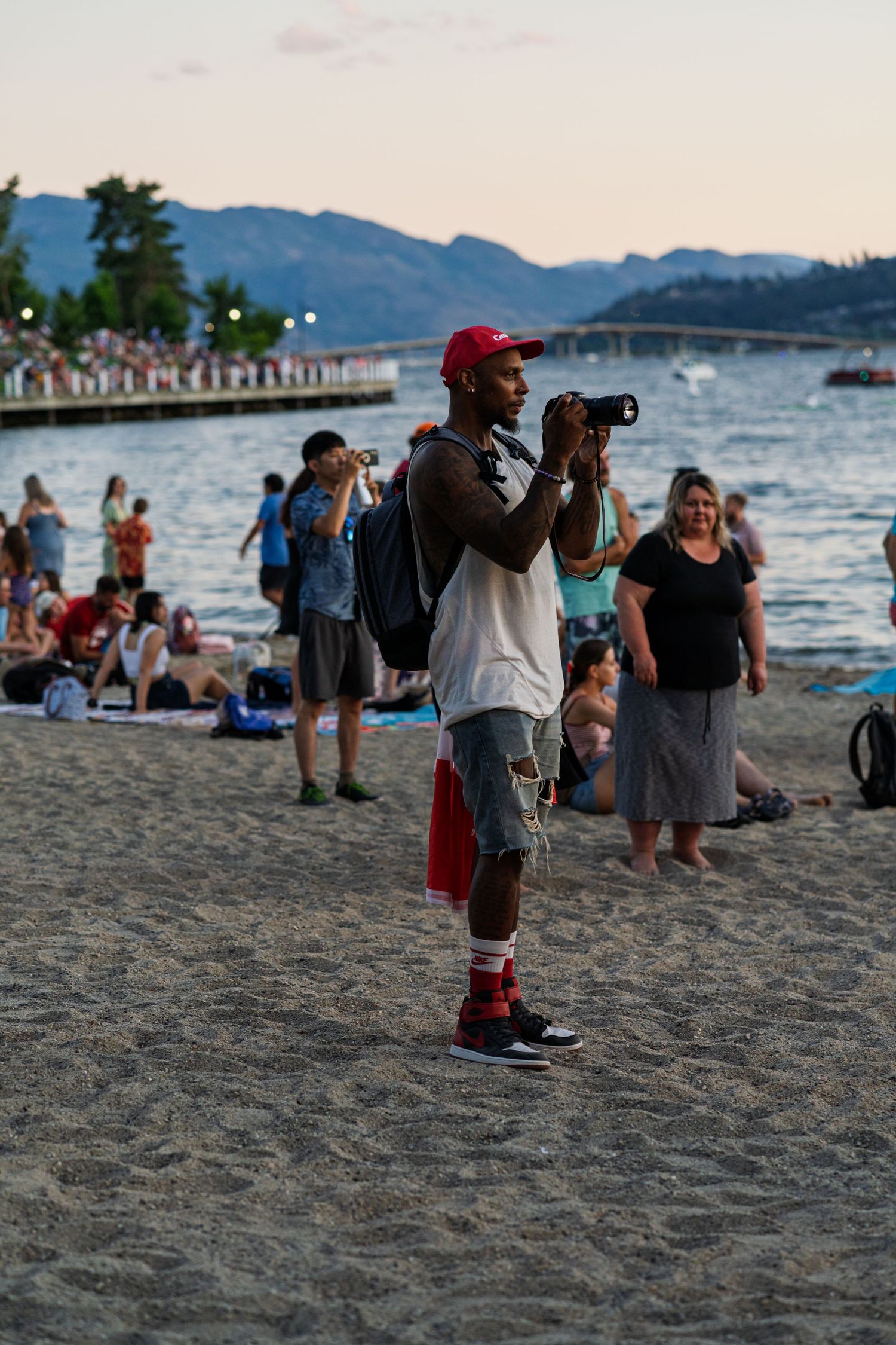 People gathered on a beach at sunset with mountains and water in the background.