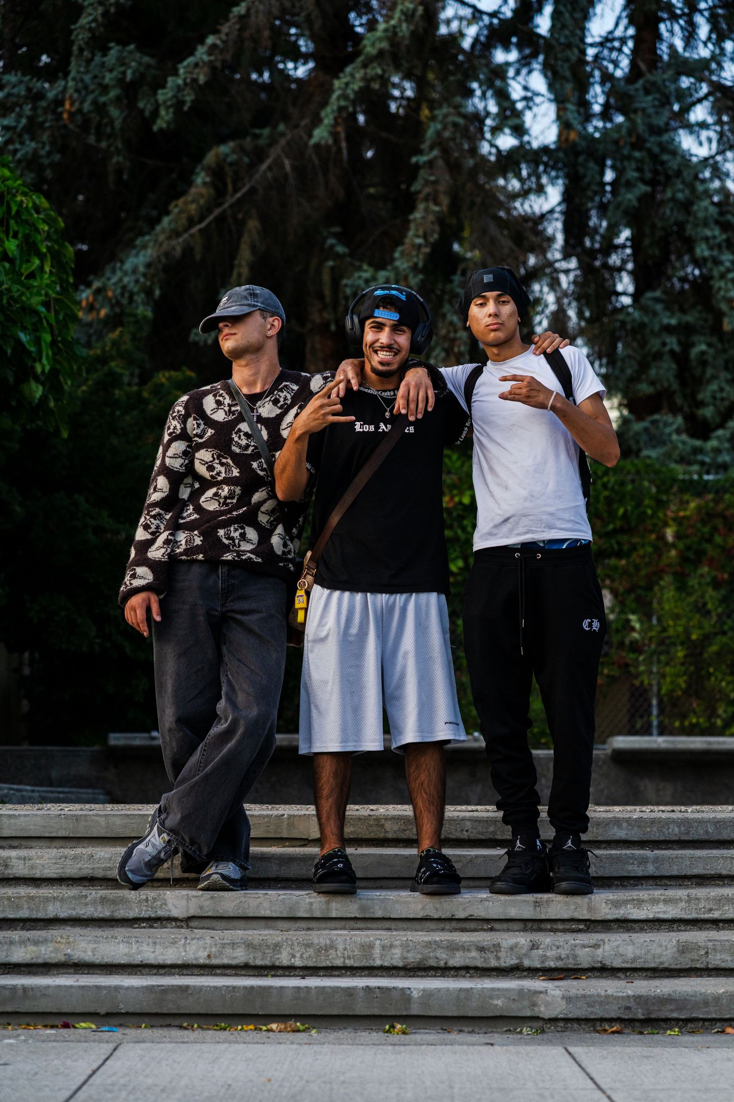 Three friends posing together on concrete steps in front of evergreen trees.