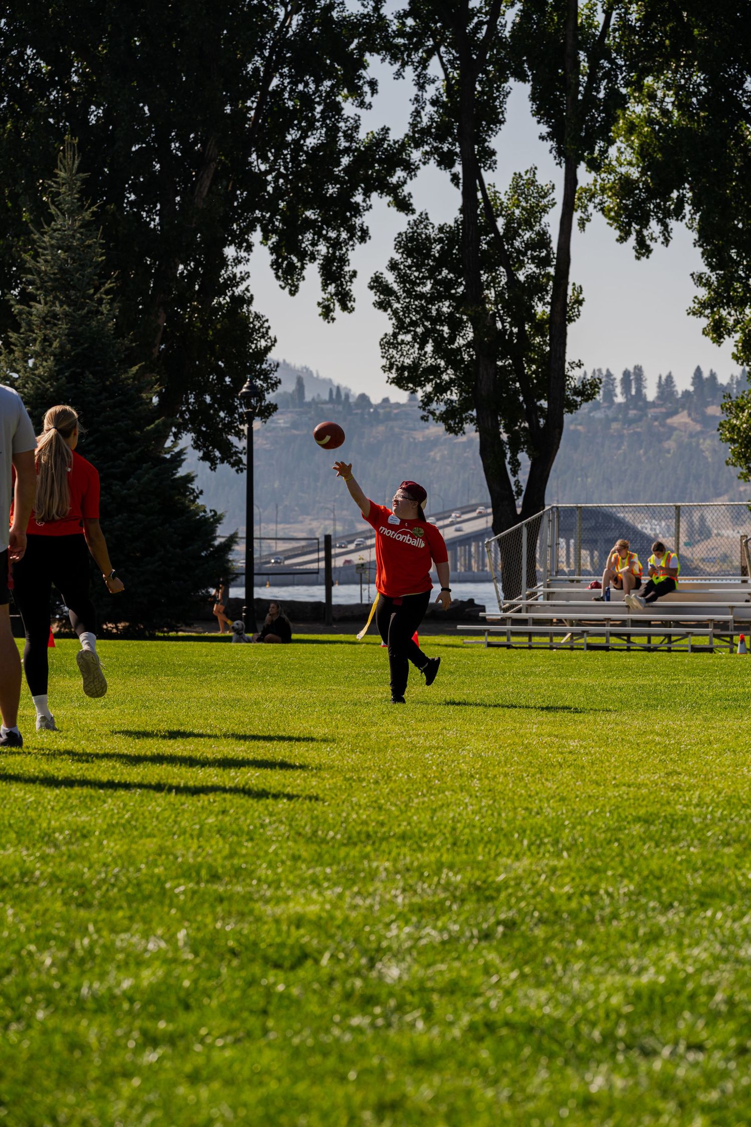 People playing sports on green field with cityscape visible in background.