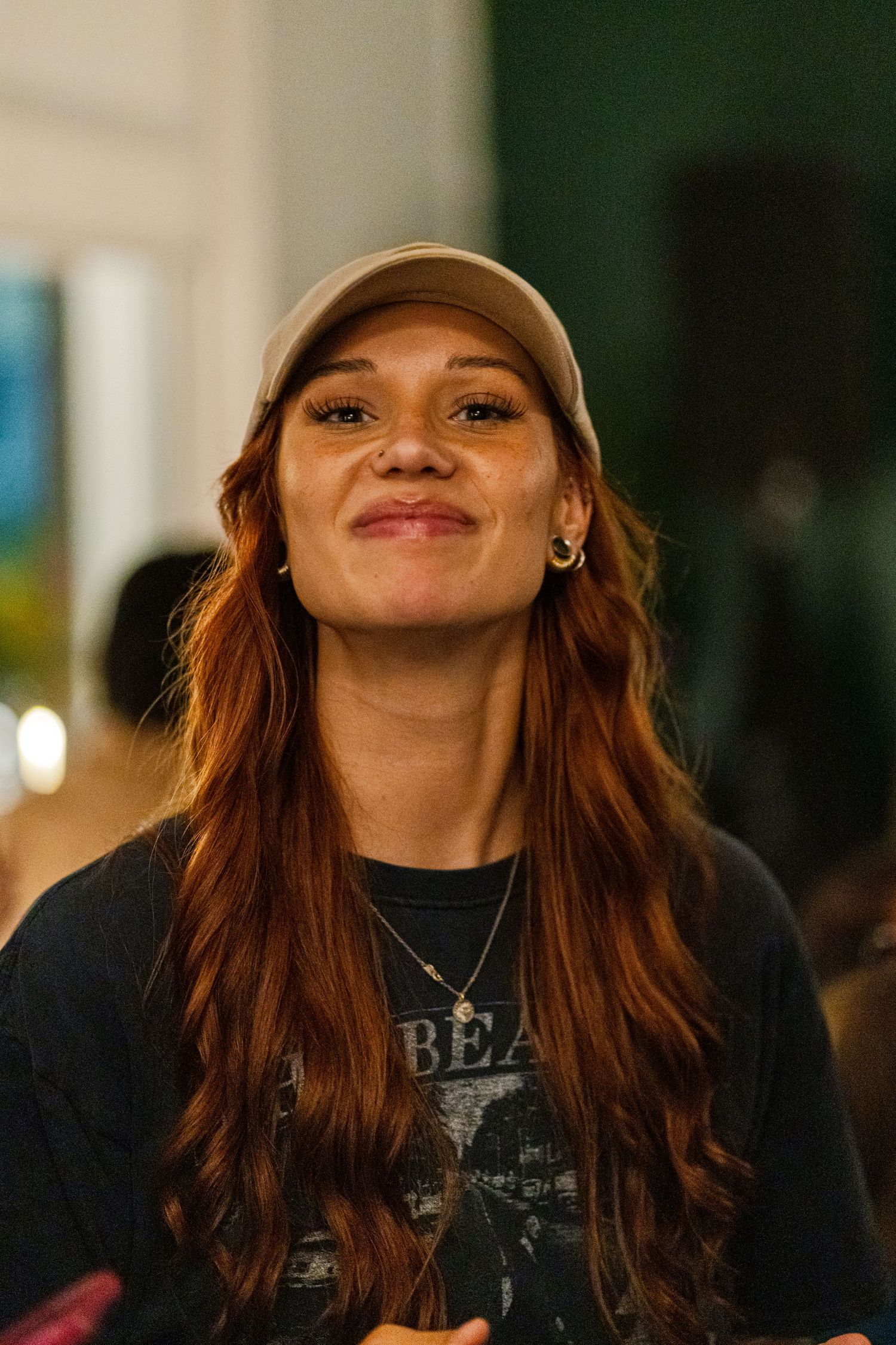 Person wearing a baseball cap and band t-shirt smiles warmly in natural lighting.