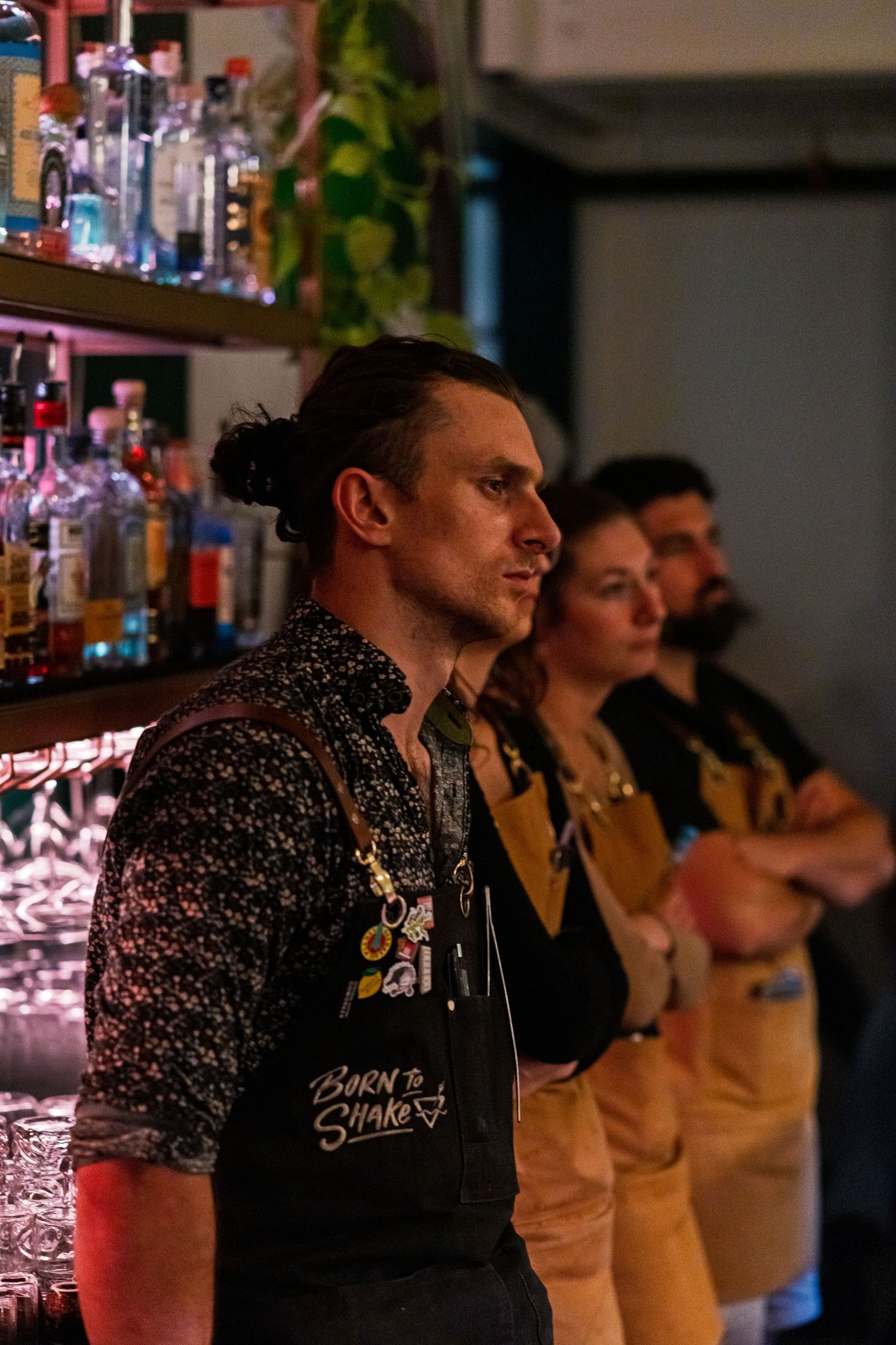 Bartenders in aprons standing behind illuminated bar counter.