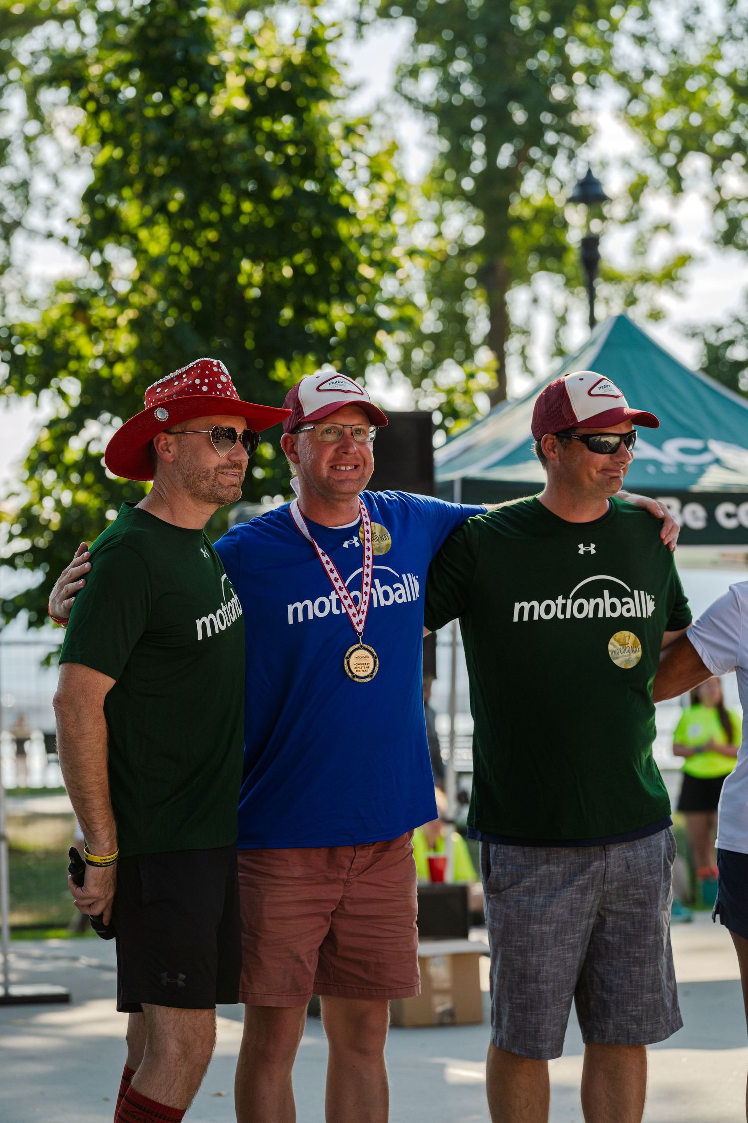 Group of friends wearing outdoor gear and branded t-shirts pose together at a summer event.