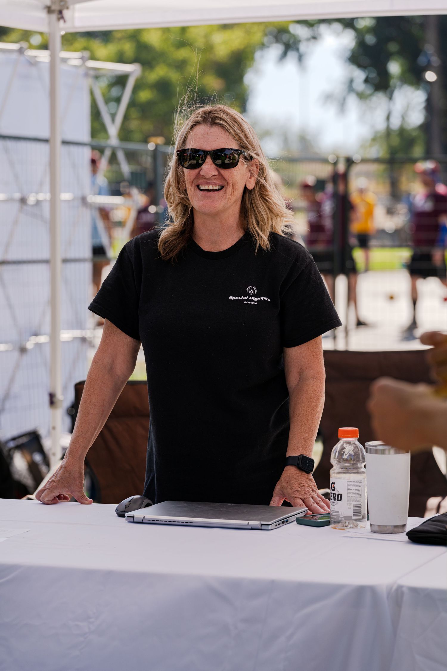 A person in a black t-shirt sitting at a white-clothed table at an outdoor event.