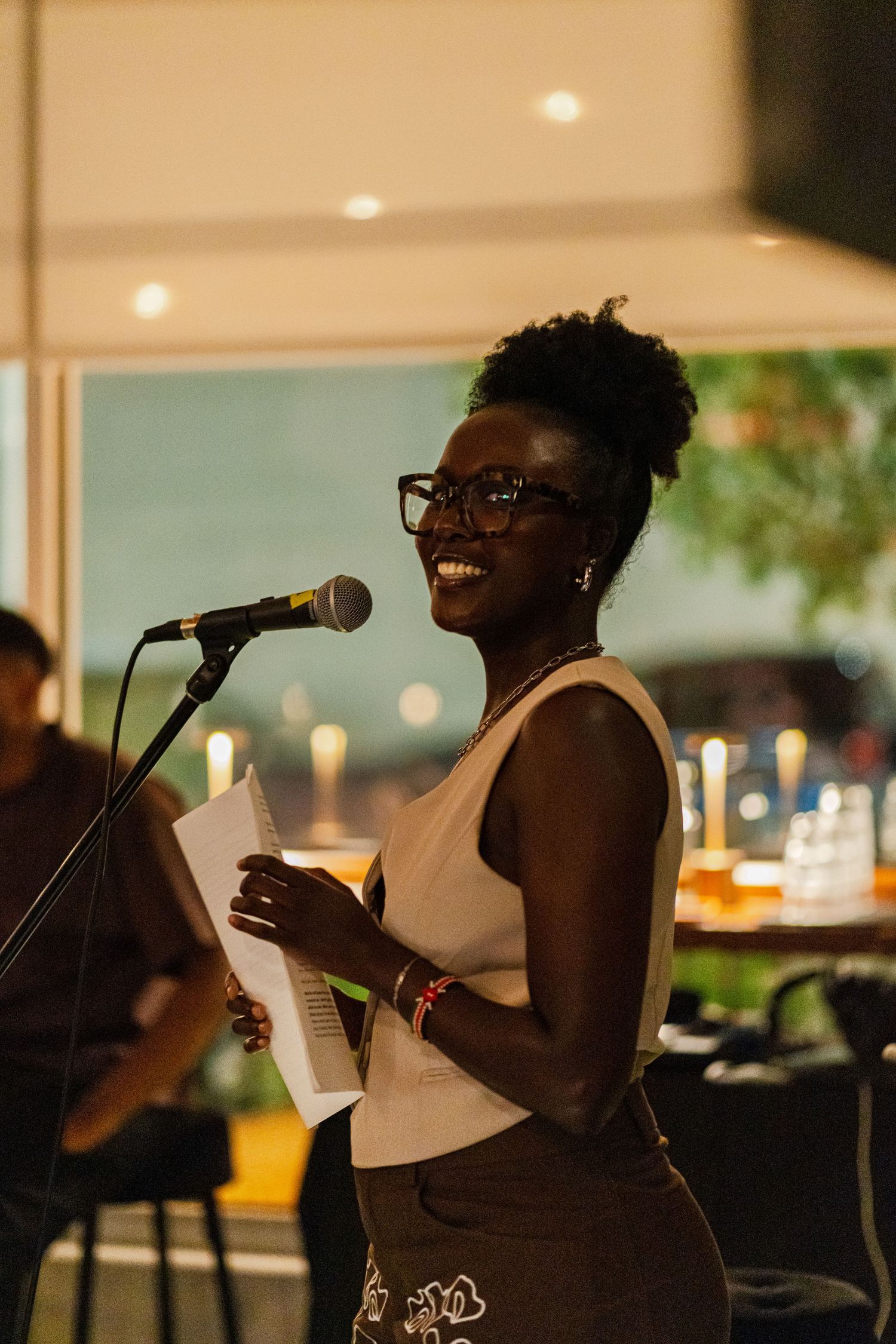 A performer sings passionately into a microphone at an indoor venue with warm lighting in the background.