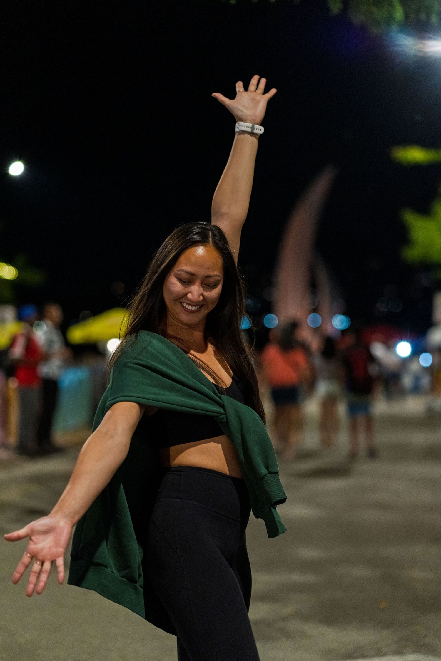 Person dancing joyfully at night with arms outstretched in an outdoor space.