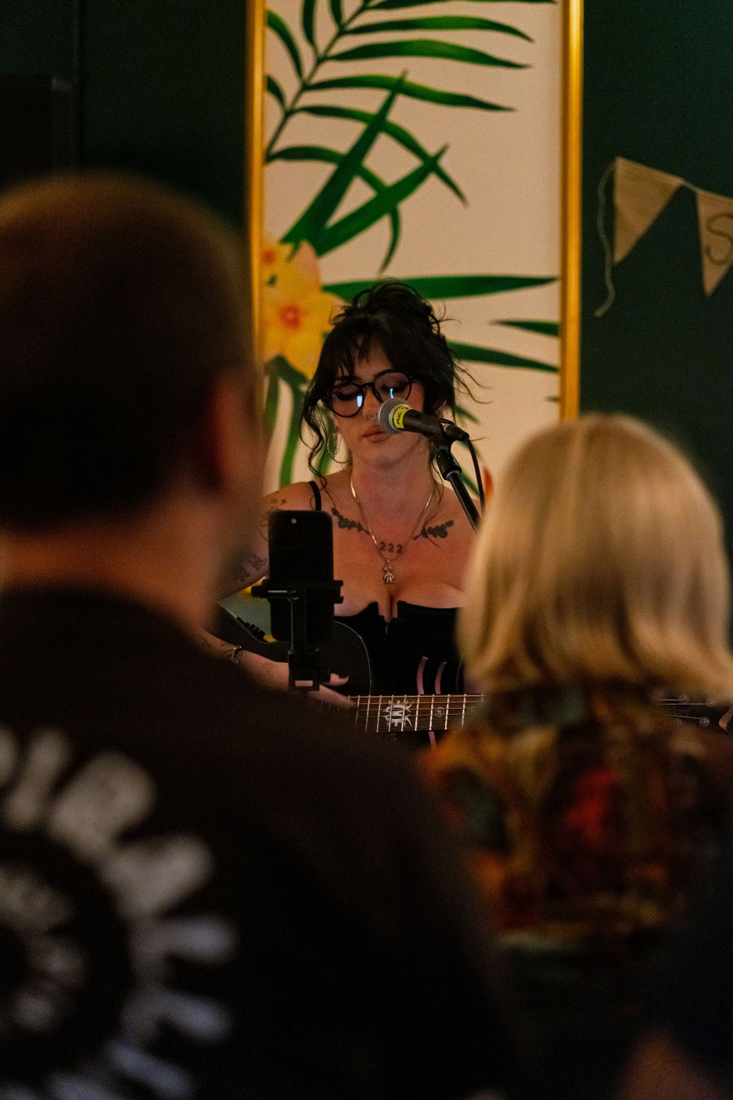 Live music performance in an intimate venue with palm leaf decorations on the wall.