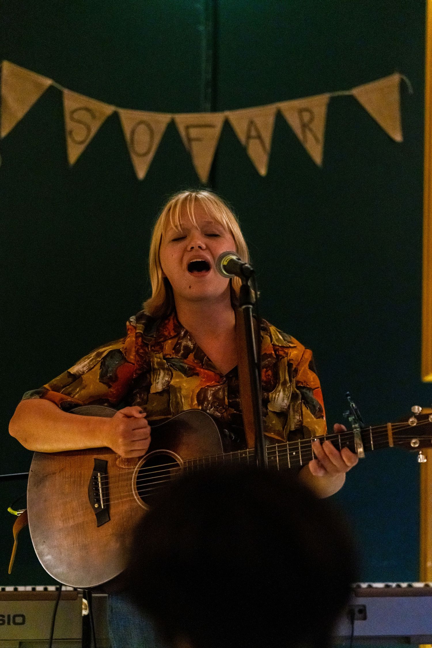 Musician performing on acoustic guitar under rustic bunting decorations in dark venue.