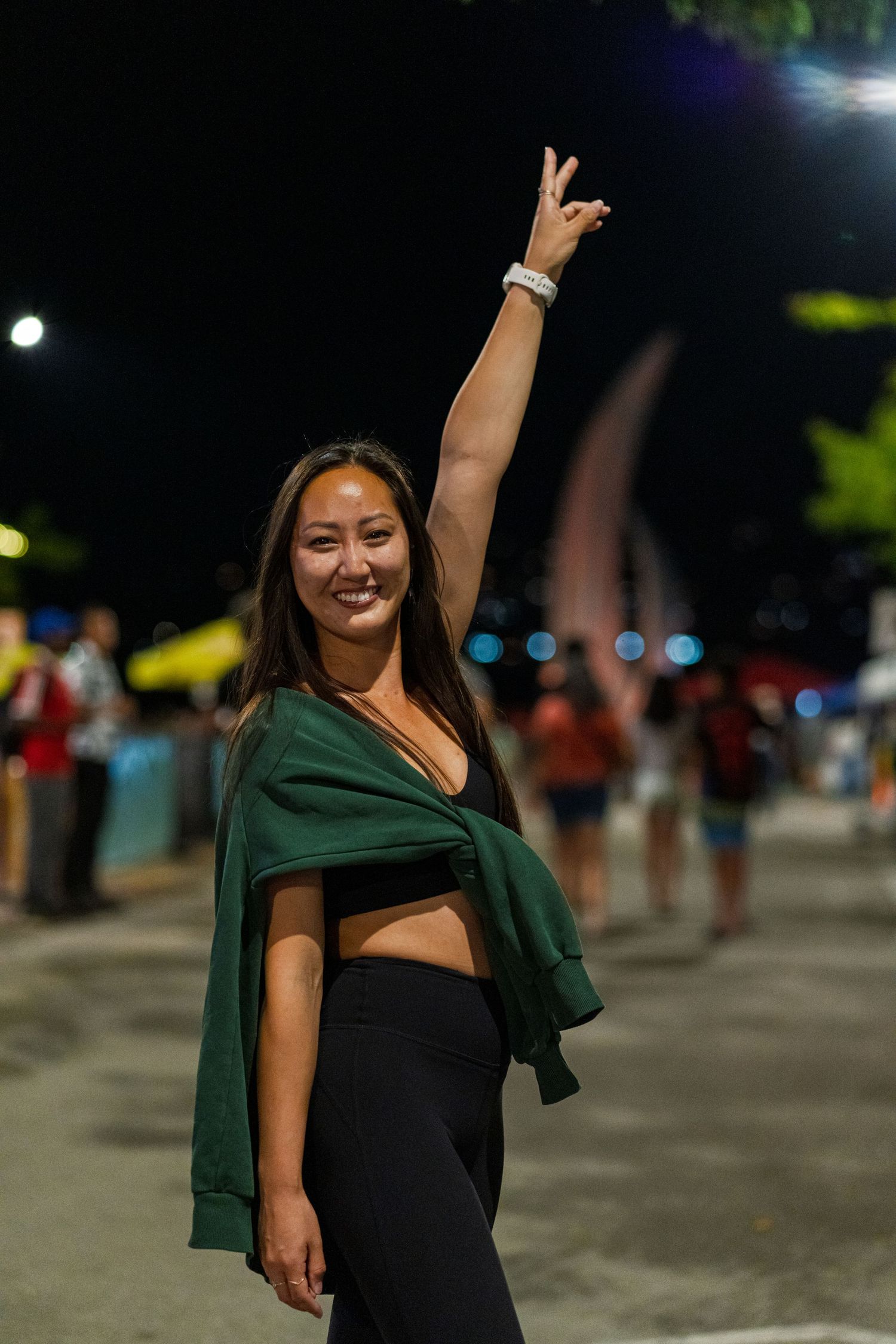 A person in a black outfit and green shawl dances joyfully at a nighttime outdoor event.