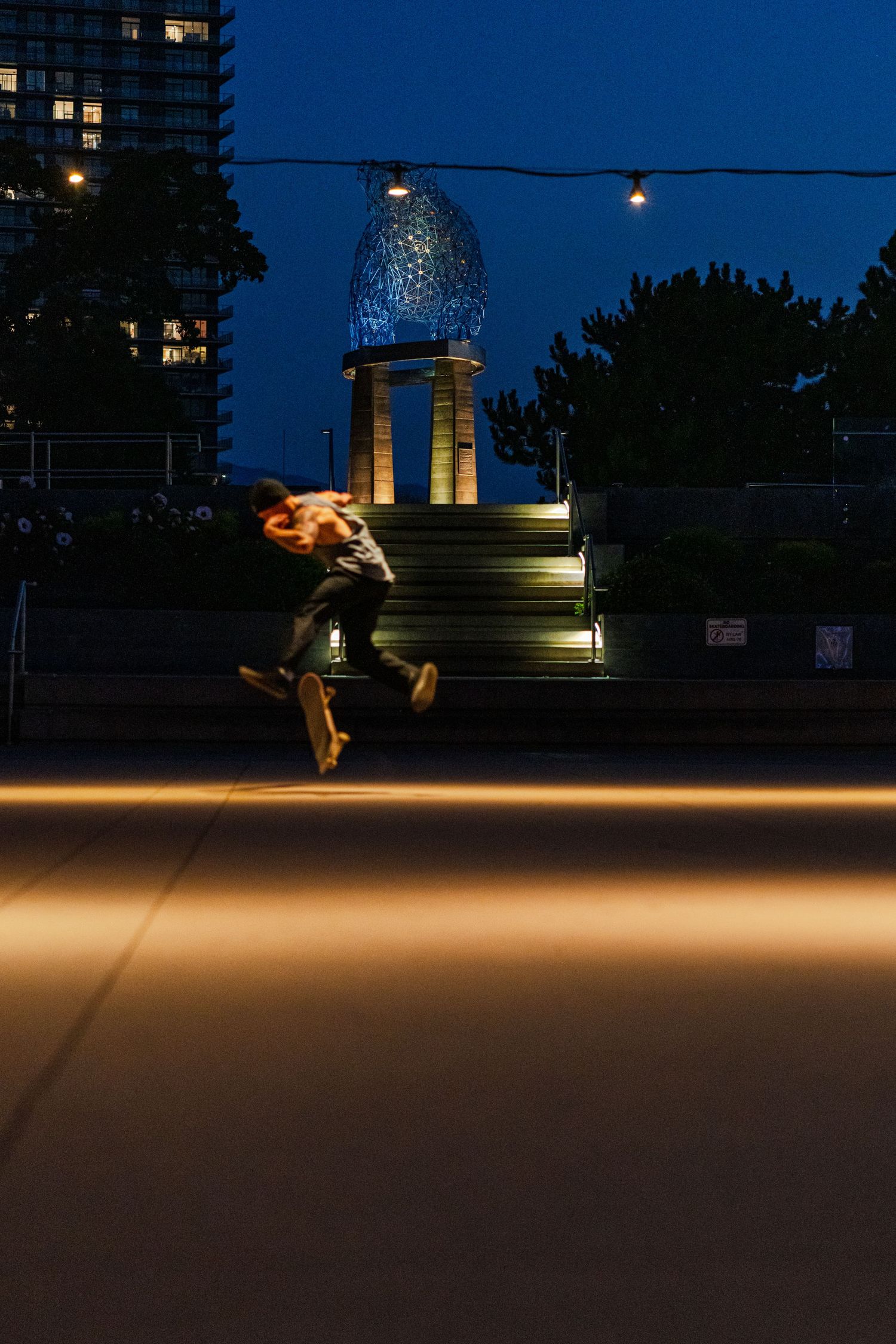 A skateboarder performs tricks against a dark blue twilight sky with city buildings in the background.