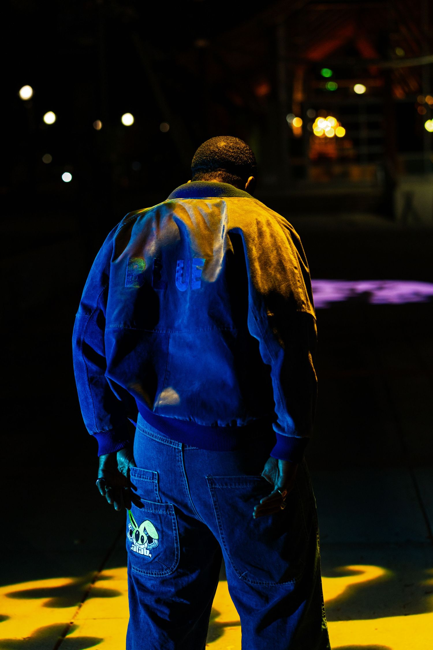Back view of person wearing bright blue clothing illuminated by yellow lights in dark setting.