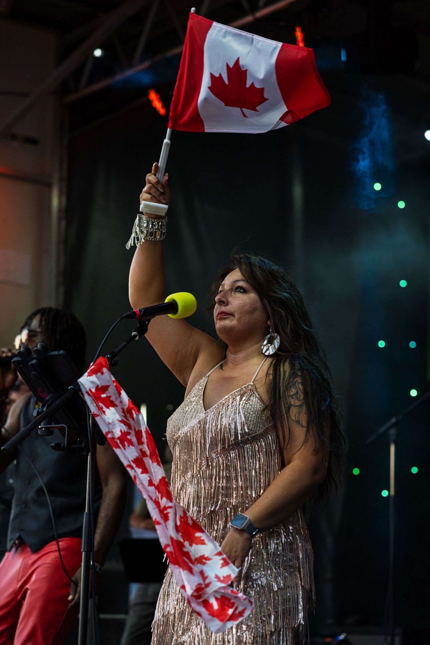 Performer in sparkly dress waving Canadian flags during stage show.