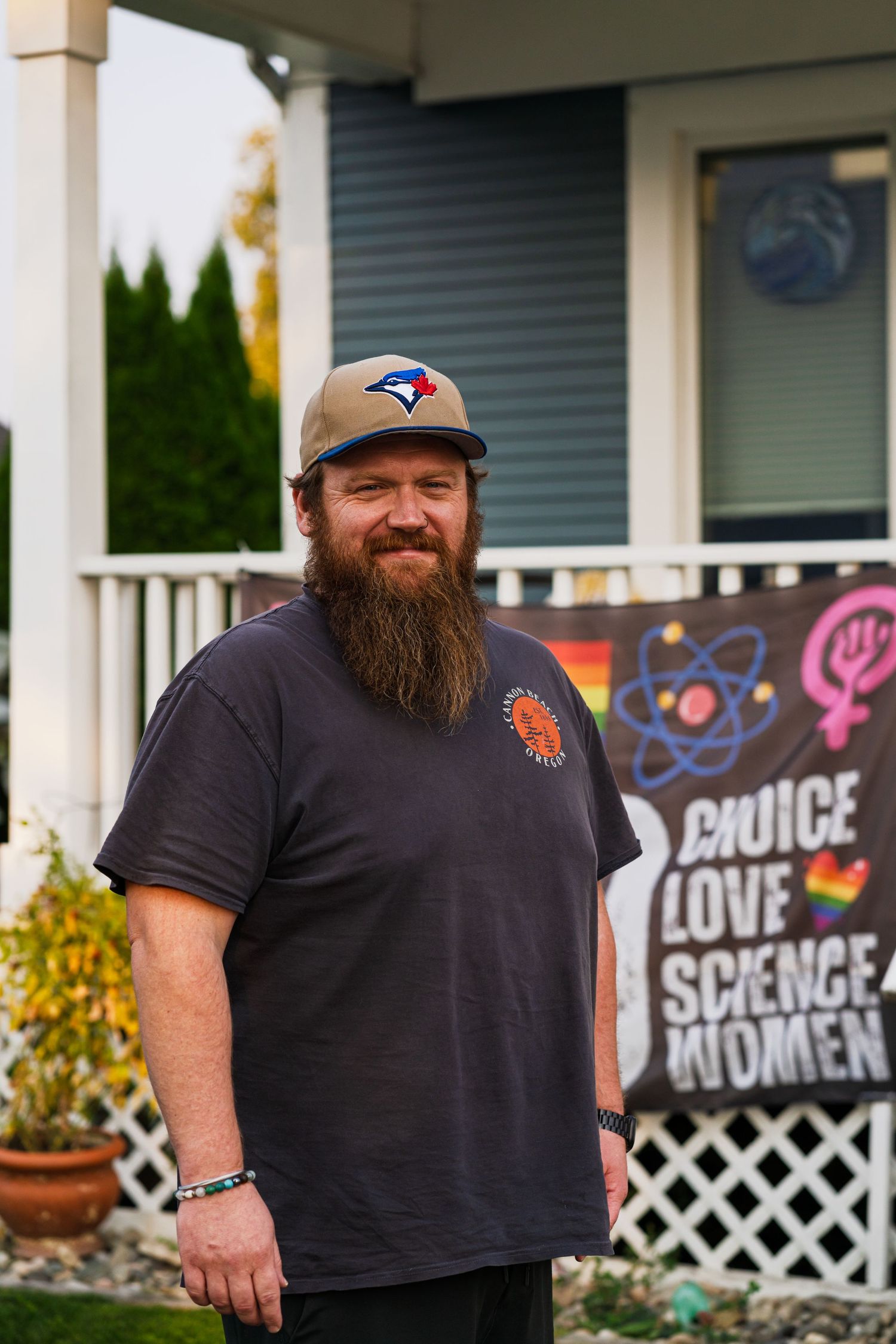A person wearing a Blue Jays cap and black t-shirt stands on a porch with a colorful sign visible in background.