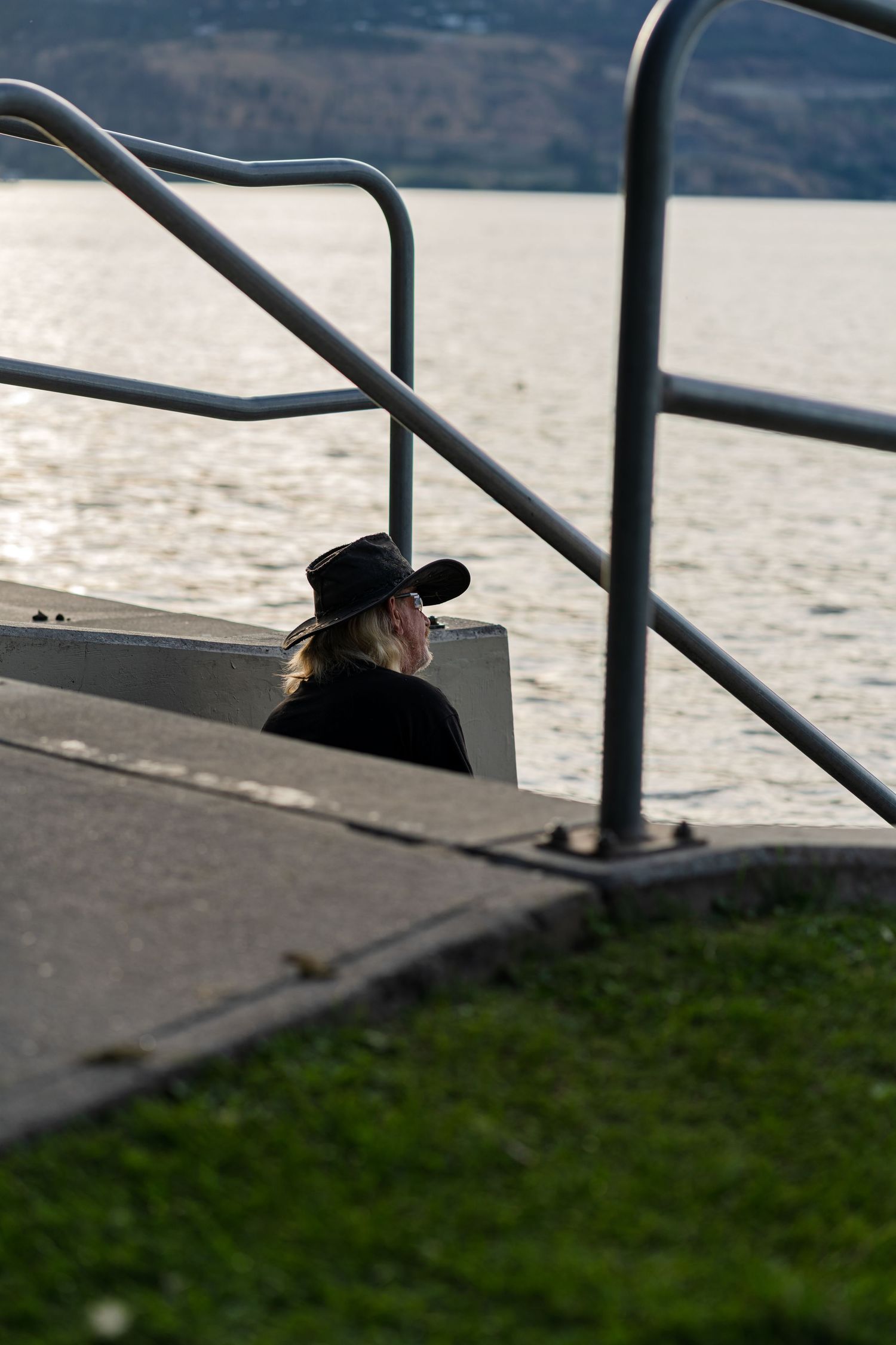 Silhouette of person behind metal railings near water at sunset.