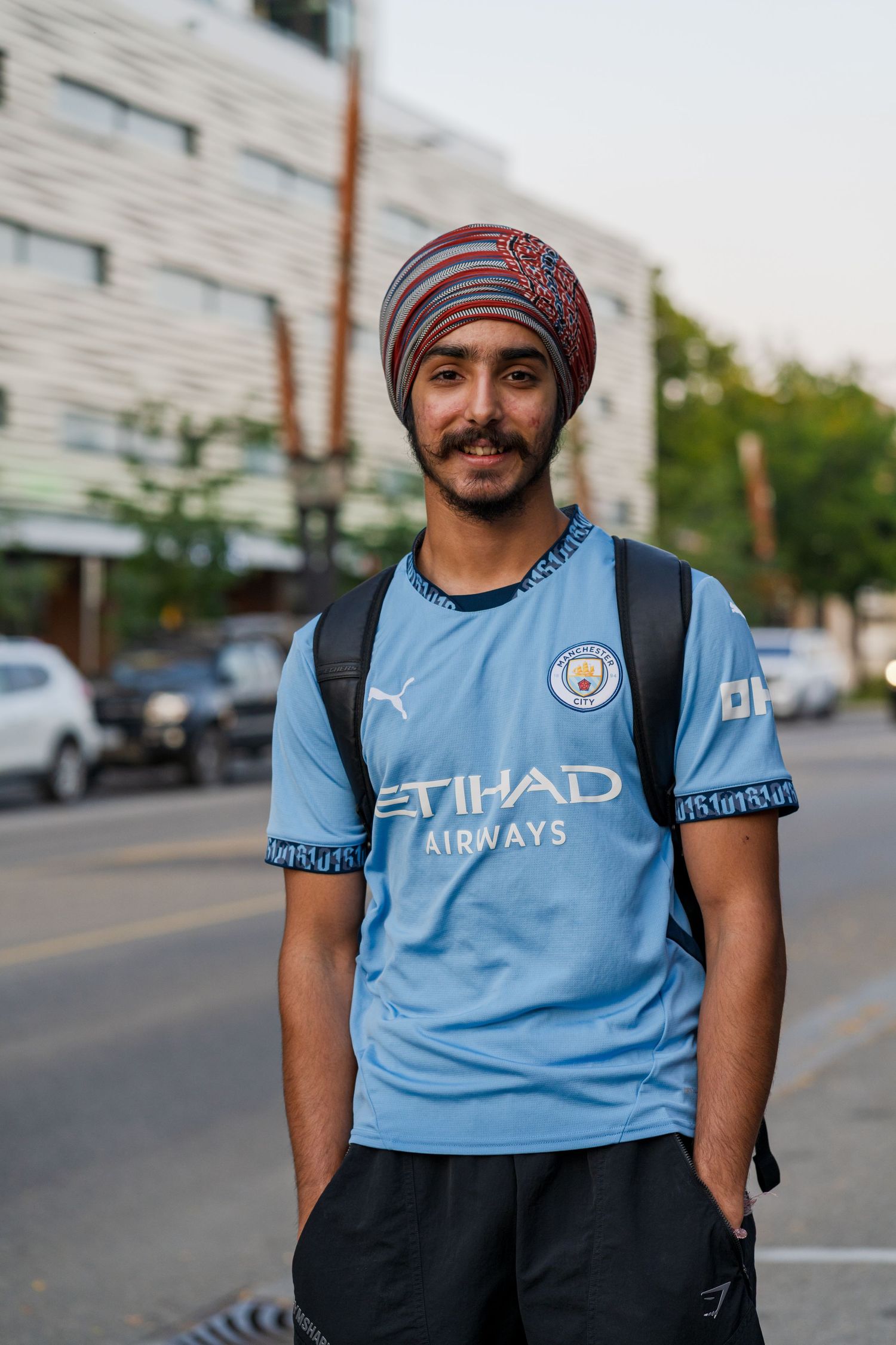 A person wearing a Manchester City jersey and striped beanie poses for a series of casual outdoor portraits.