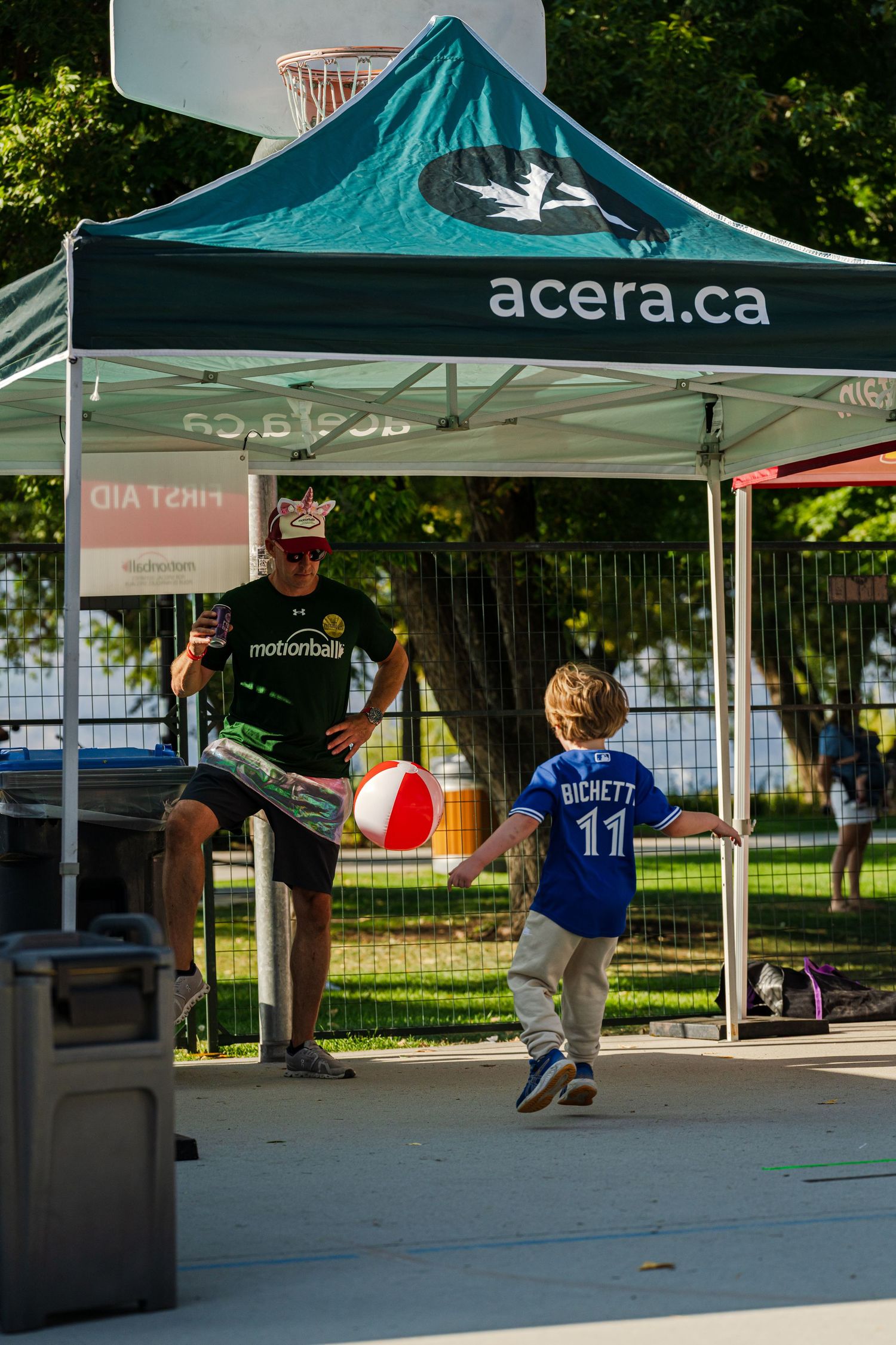 Child plays with a ball under a teal promotional tent at an outdoor event.