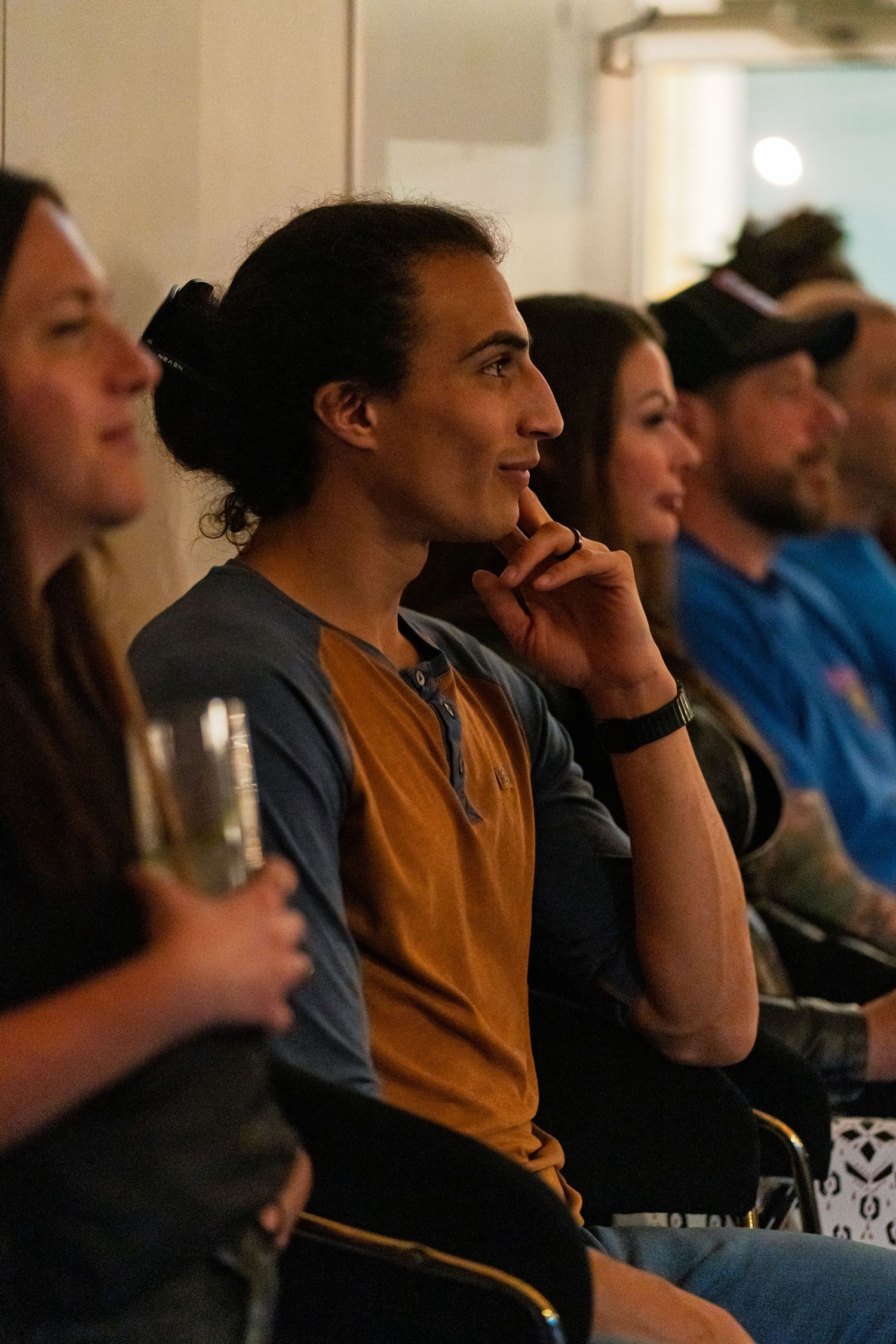 Group of people watching performance in dimly lit venue with person in brown shirt in focus.