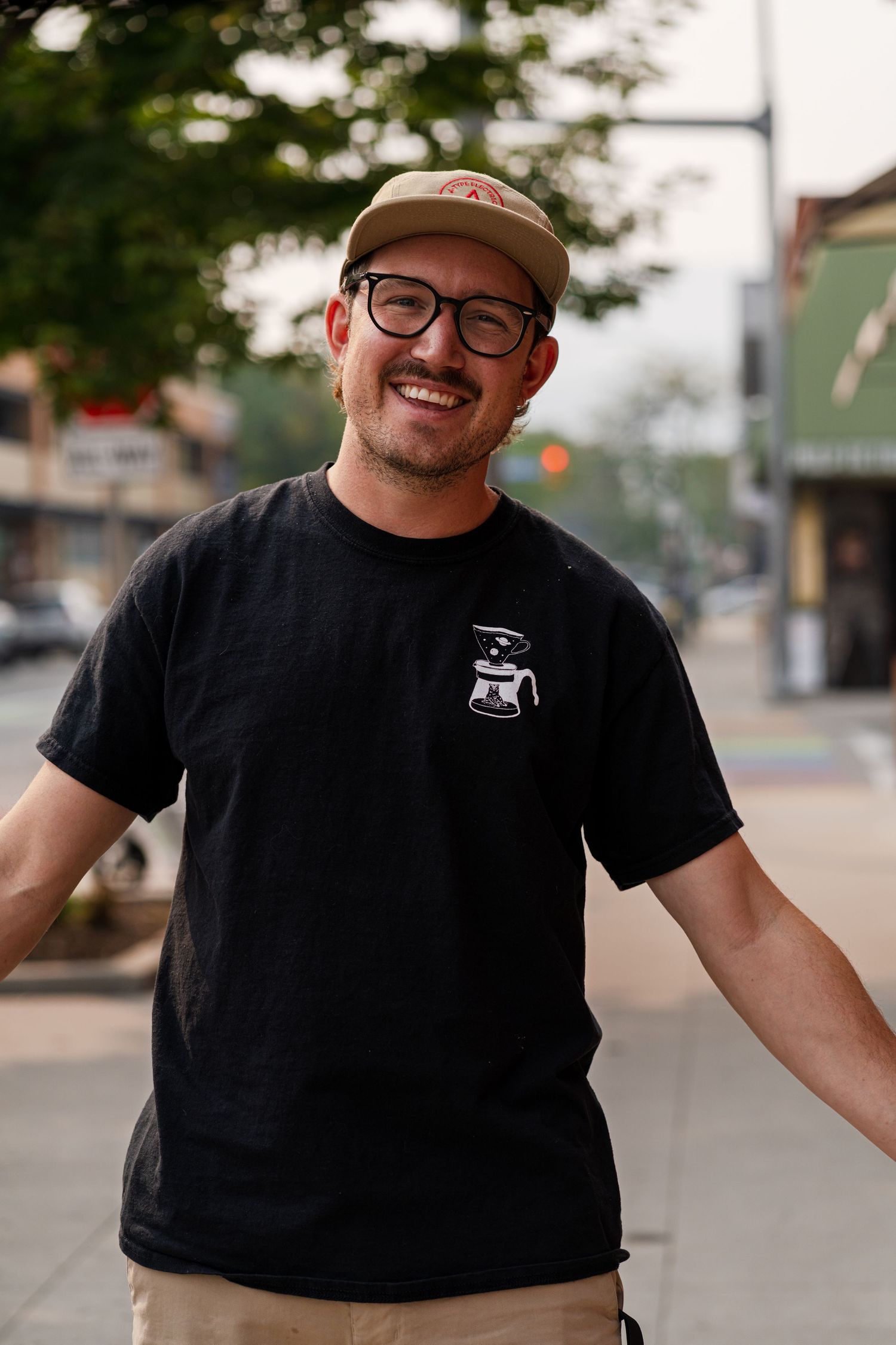 Person in black t-shirt and cap smiling on a city street.