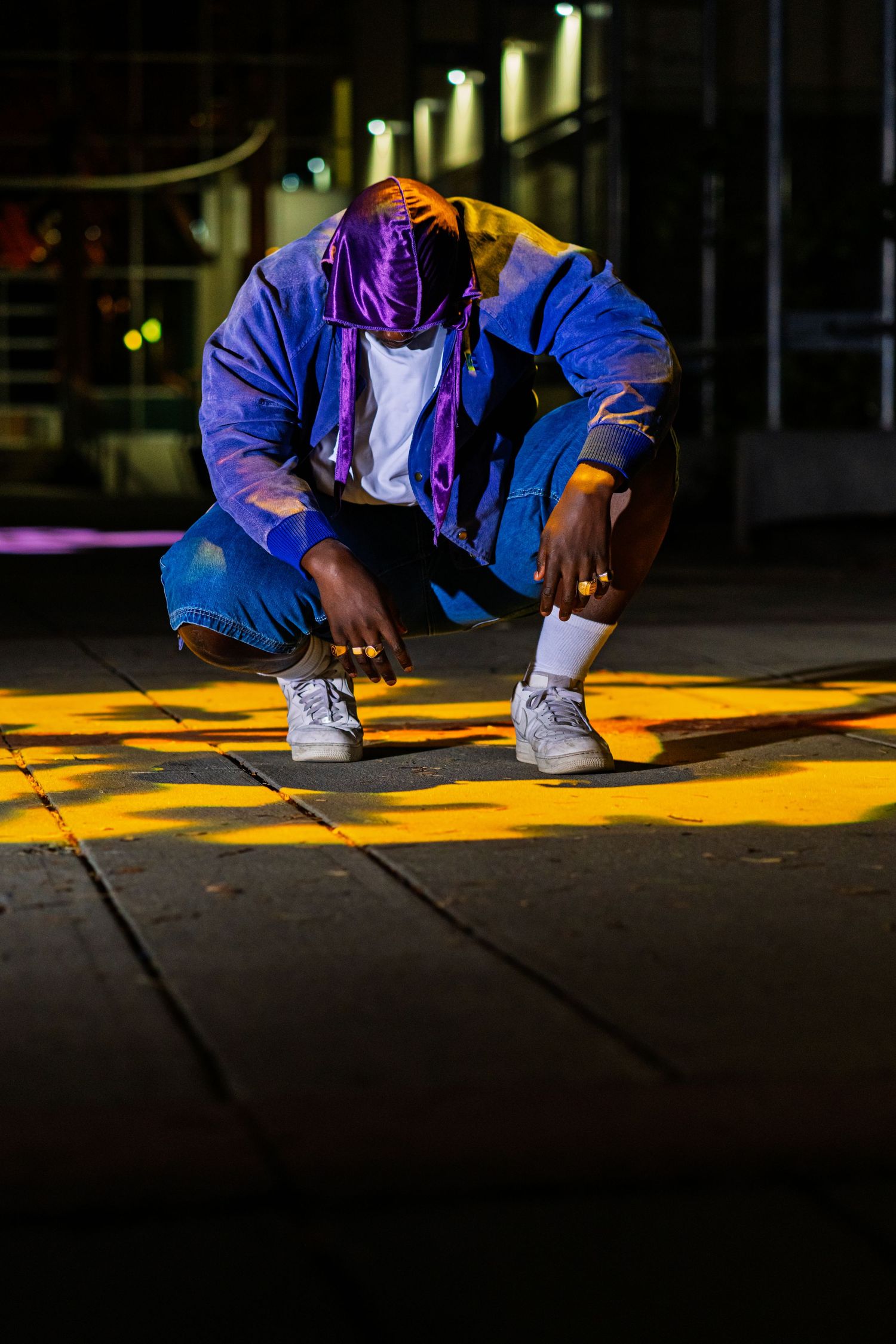 Person in blue jacket crouches down to paint bright yellow lines on dark pavement at night.