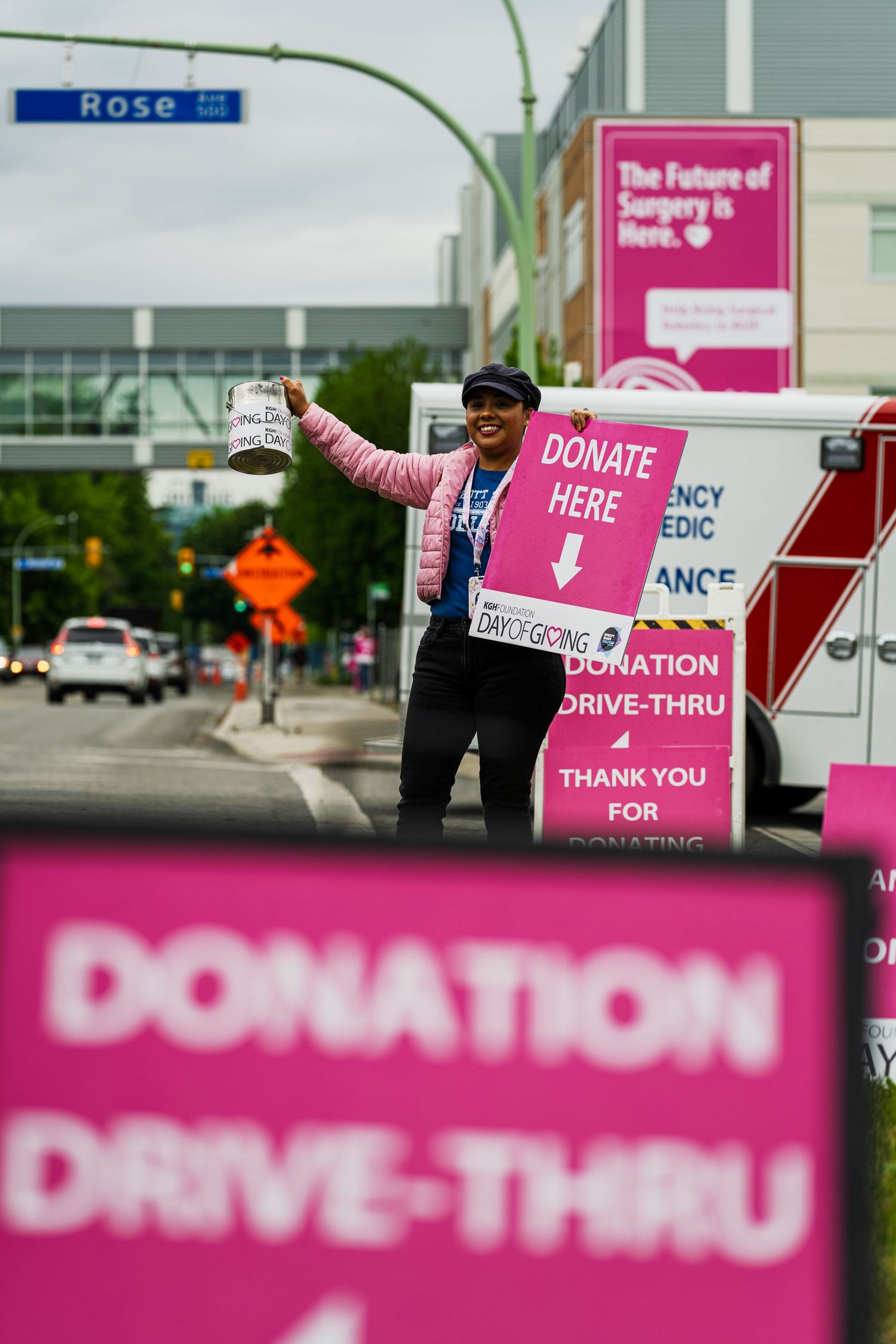 Person holding donation sign at pink-themed drive-thru fundraising event on Rose Street.