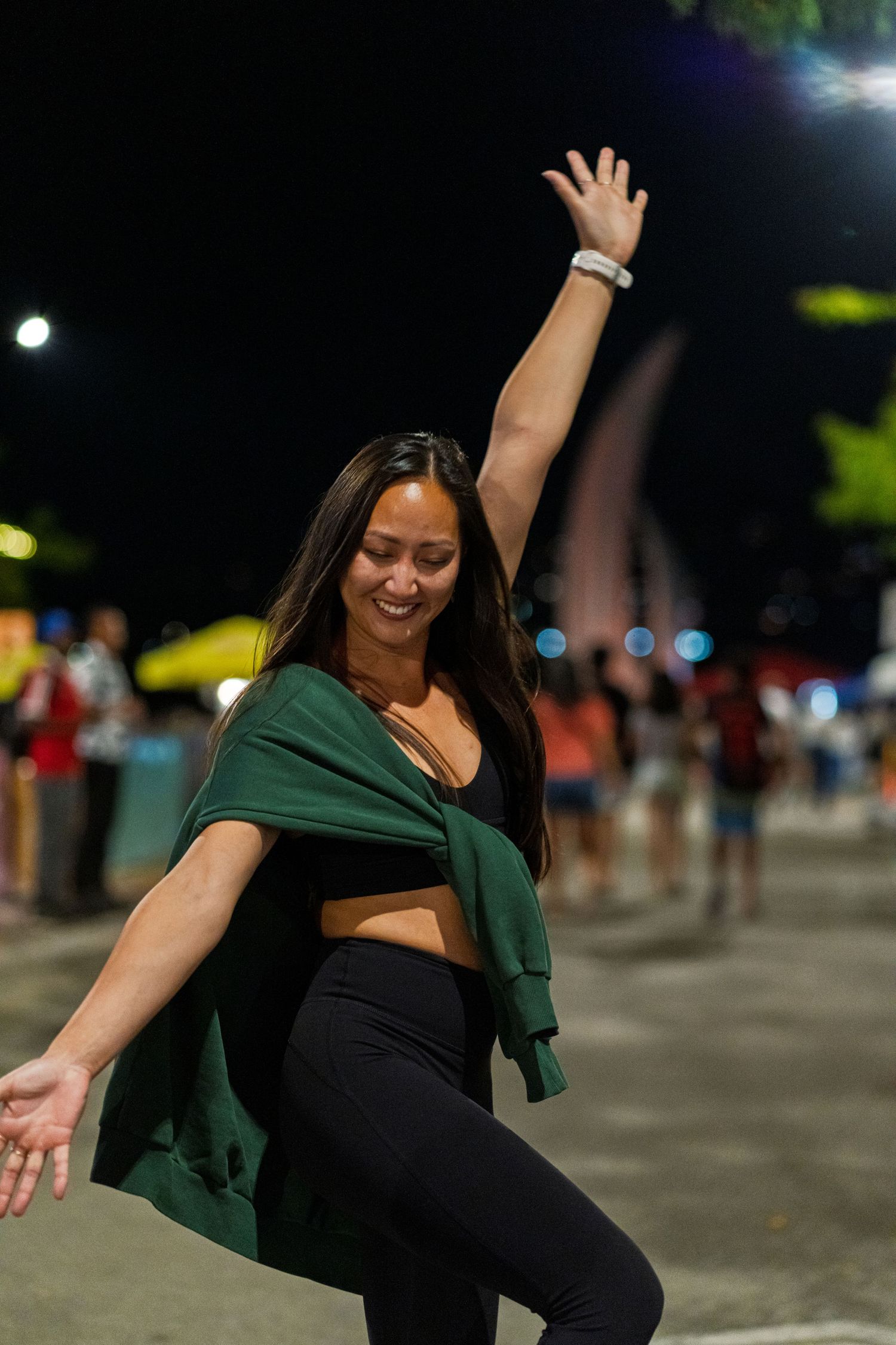 Woman in black and green outfit dancing energetically at night with city lights in background.