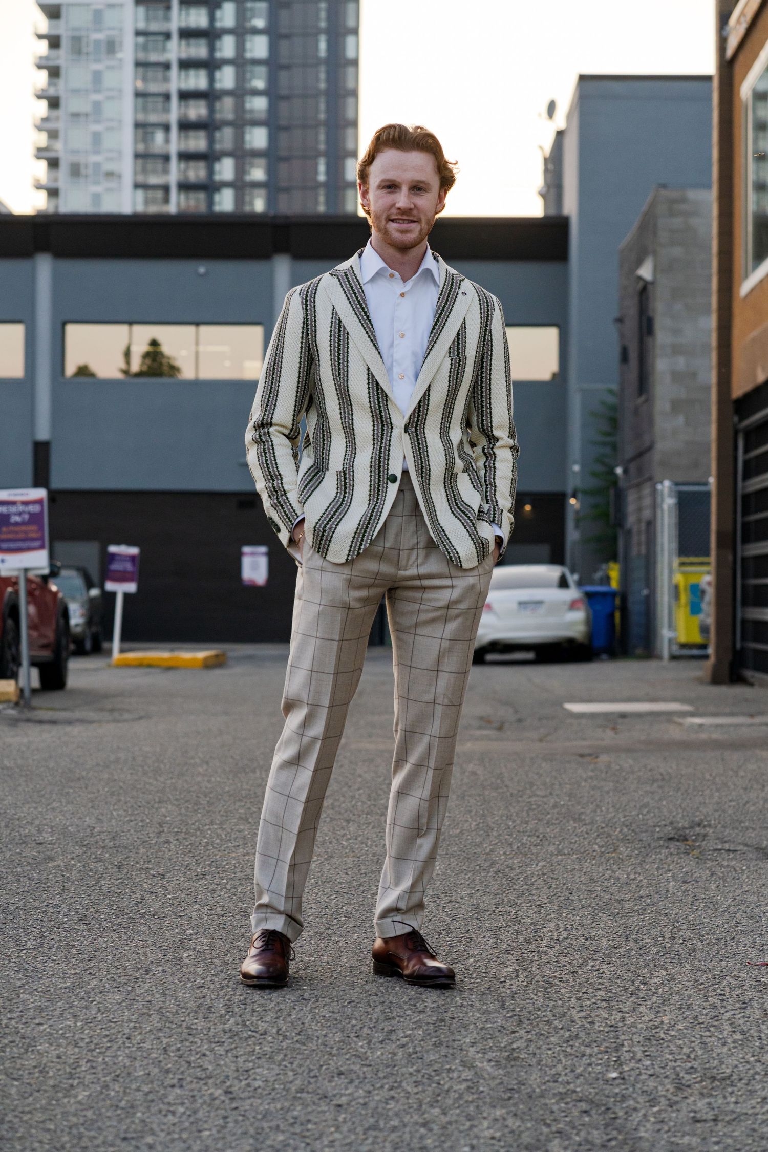 Person wearing striped blazer and dress pants poses in an urban parking lot setting.