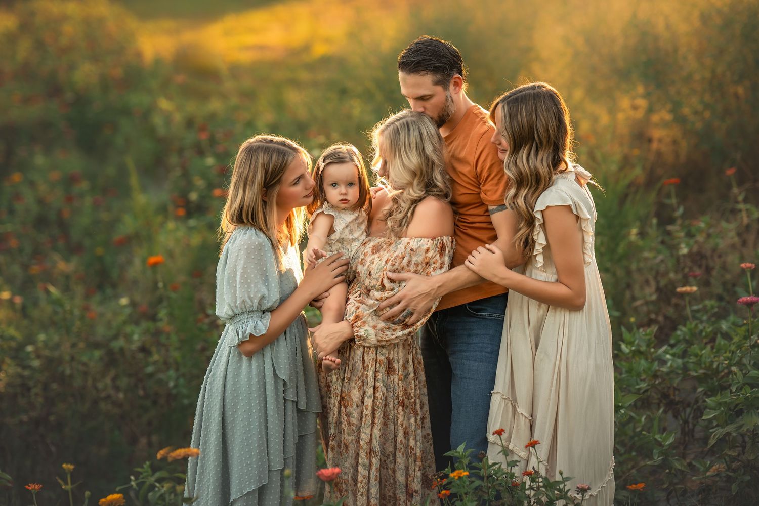 Family embraces in a golden flower meadow during sunset with warm glowing light in the background.