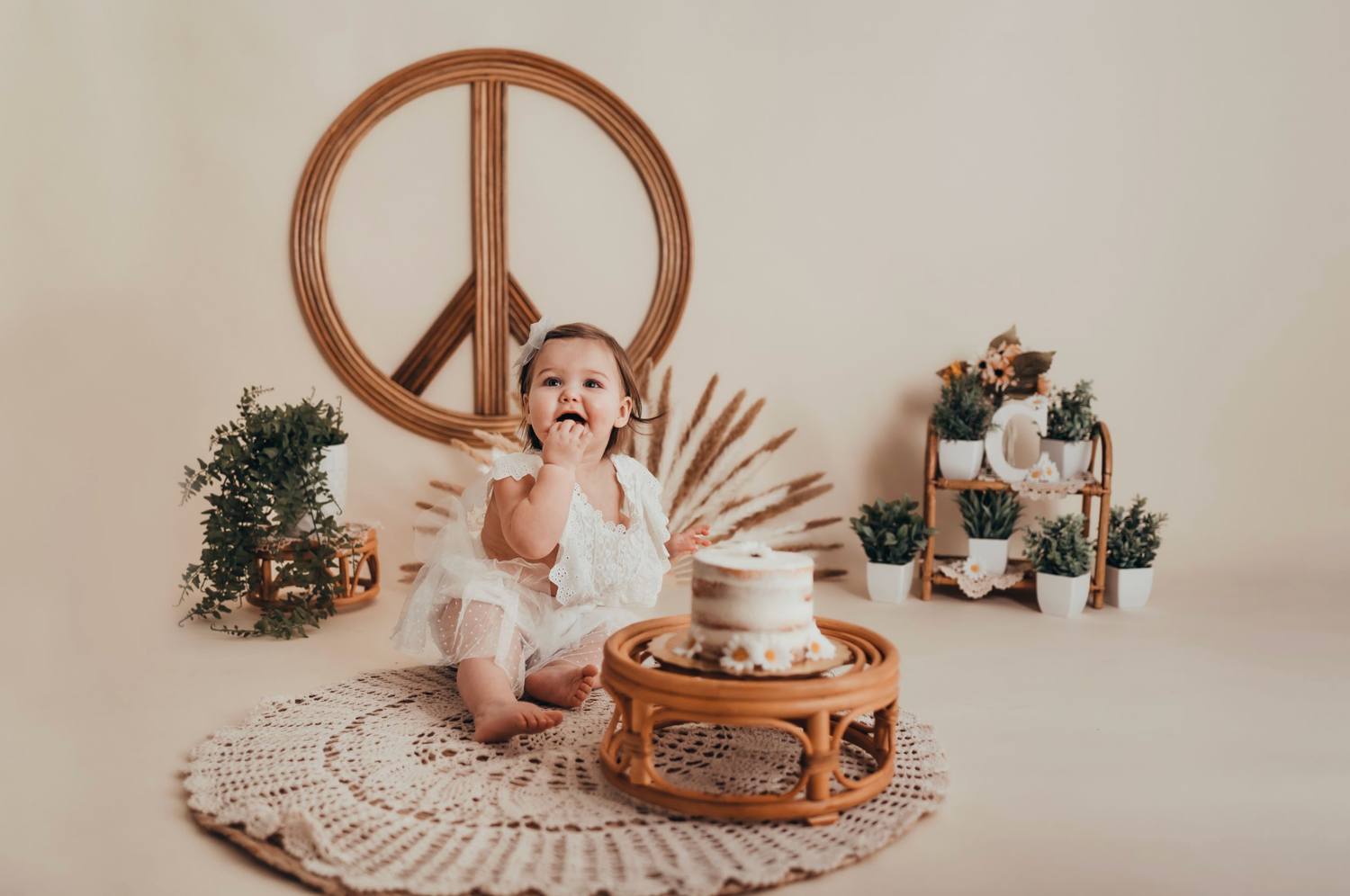 Baby's first birthday cake smash with boho decor, peace sign, and white cake on rattan table.