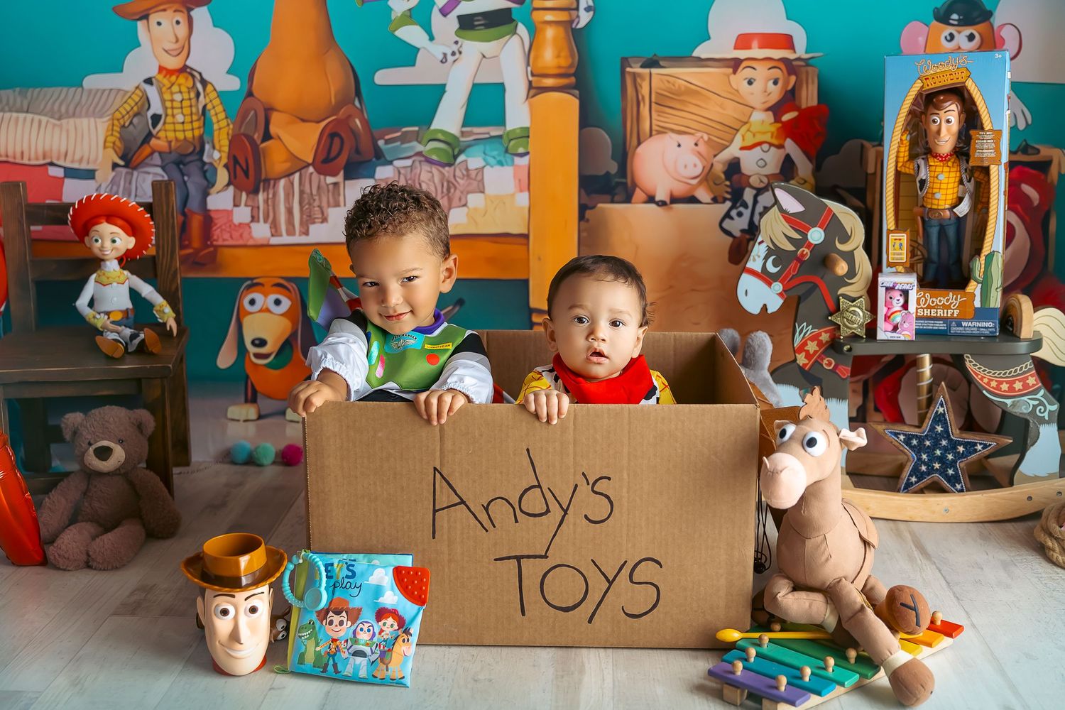 Dos bebes dentro de una caja vestidos de Woody y Buzz Lightyear la caja dice Andy's Toys sesion fotografica inspirada por Toy Story