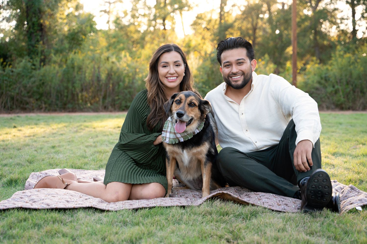 Couple sitting on picnic blanket outdoors with their mixed breed dog during golden hour sunset in nature.