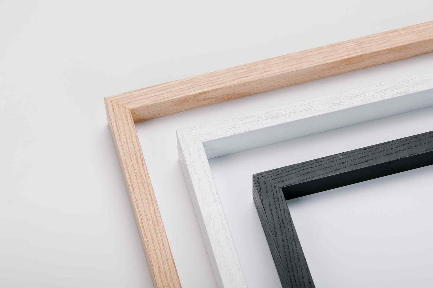 Three wooden picture frames in natural, white, and black finishes stacked diagonally on a white background.