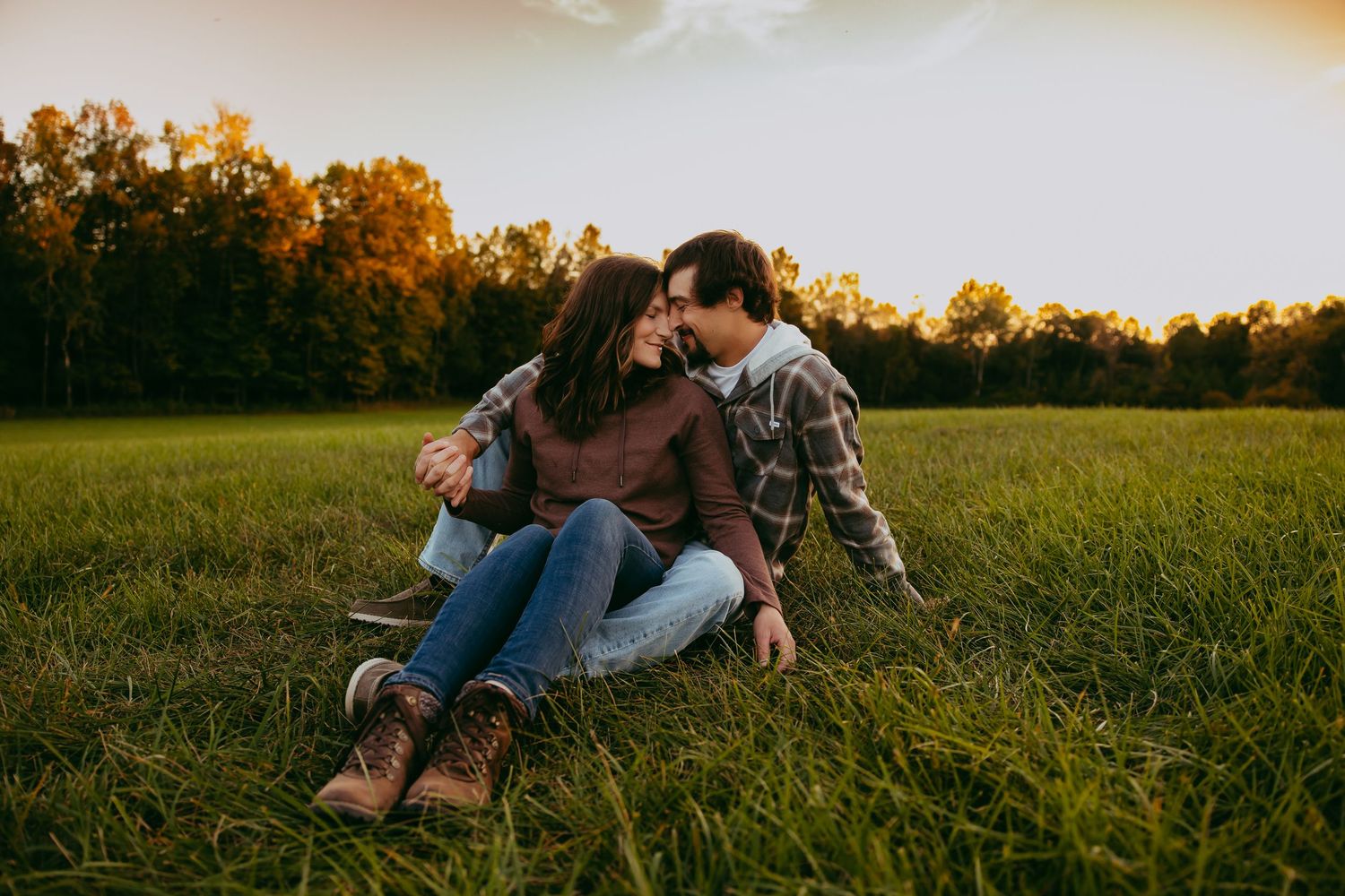 A couple relaxes together in a golden sunlit meadow during sunset, creating a romantic outdoor moment.