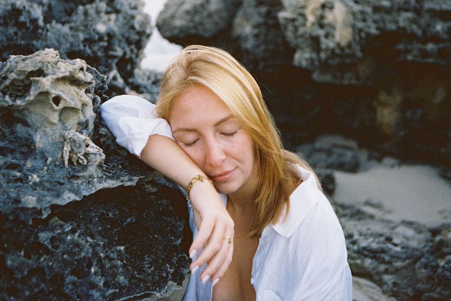 Emotive portrait of a woman embracing stillness on the rocks — shot on film at Mettam’s Pool, Western Australia.