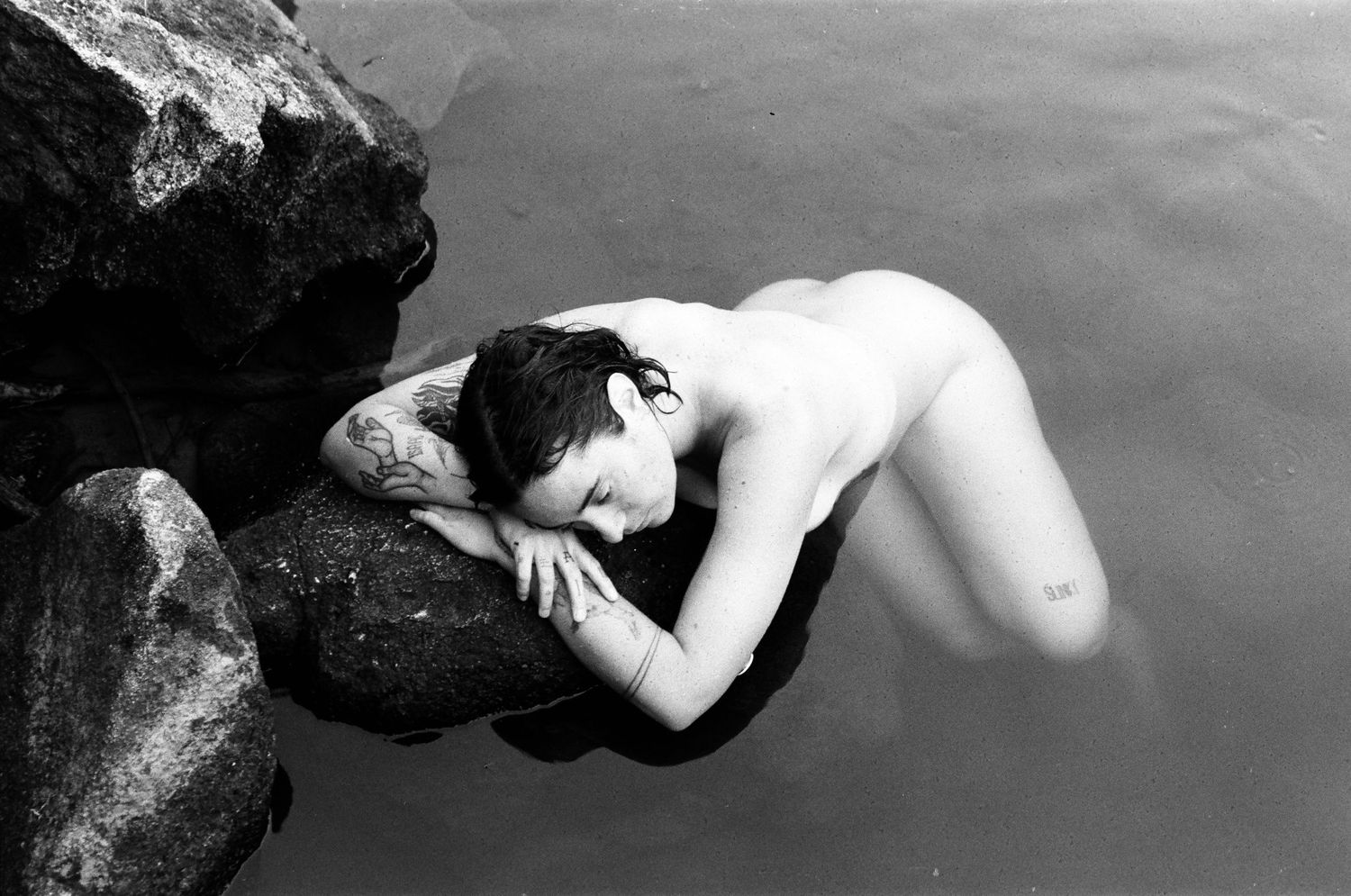 Woman resting in a still, shallow river pool surrounded by smooth rocks — soulful film photography in the Perth Hills.