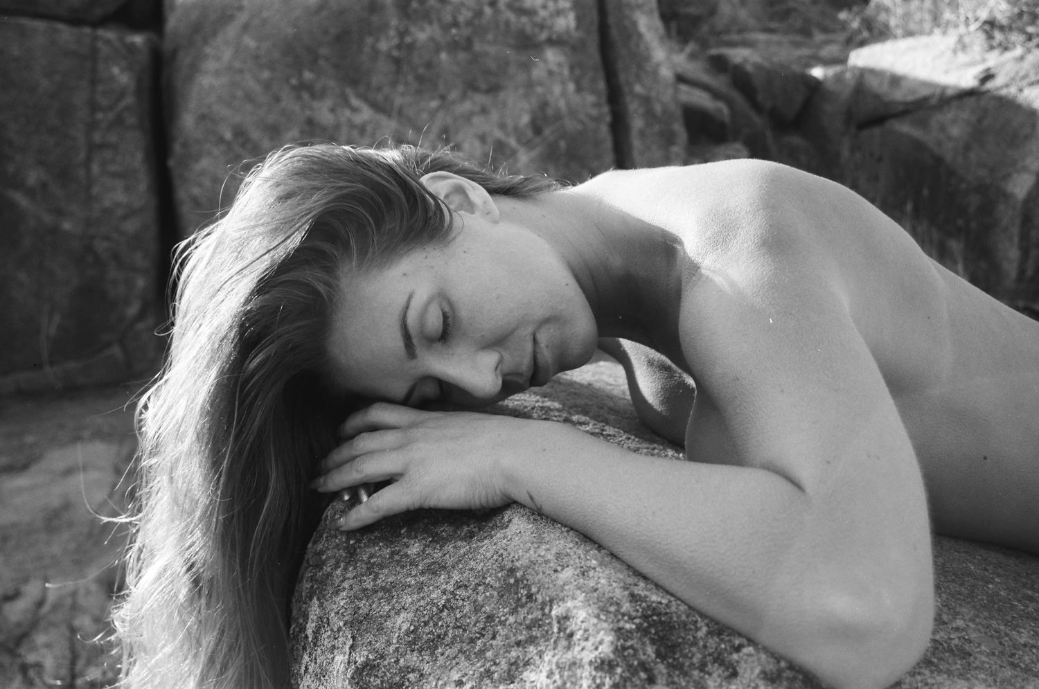 Woman reclining on a warm boulder beside a running stream — raw and grounding film photography in Western Australia’s hills.