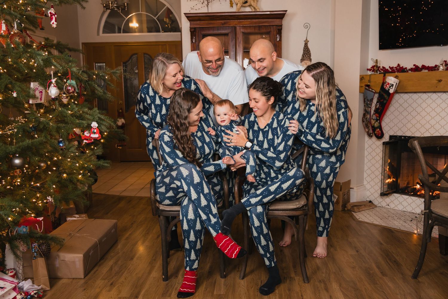 Family wearing matching blue snowflake pajamas gather around a decorated Christmas tree in cozy living room setting.