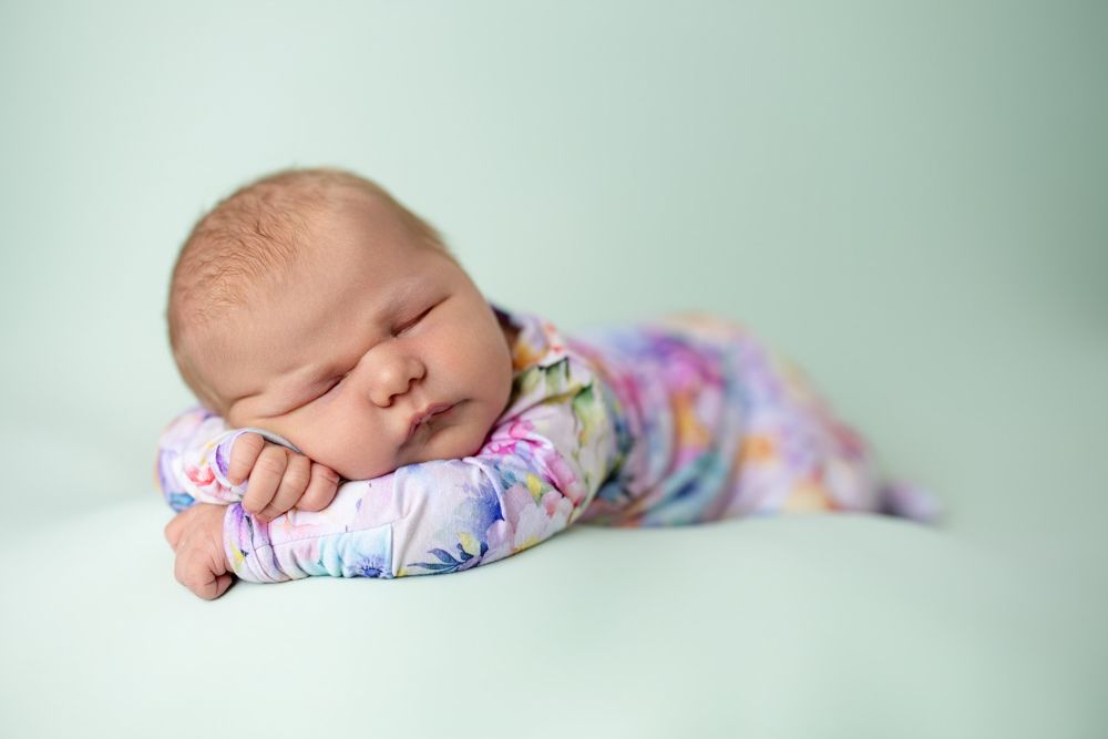 Sleeping newborn baby wearing floral print outfit rests peacefully on mint green background.