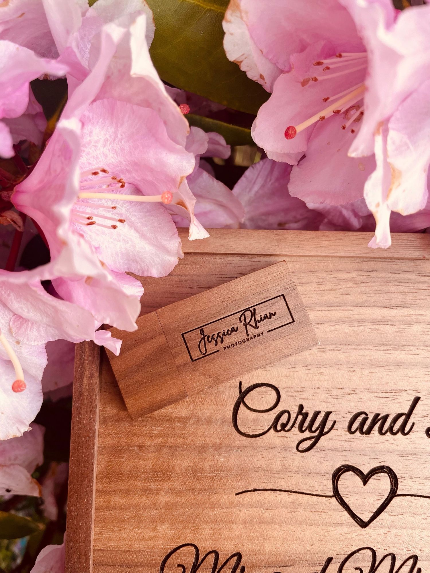 Close-up of wooden box corner with maker's mark and wedding inscription among pink blooms.