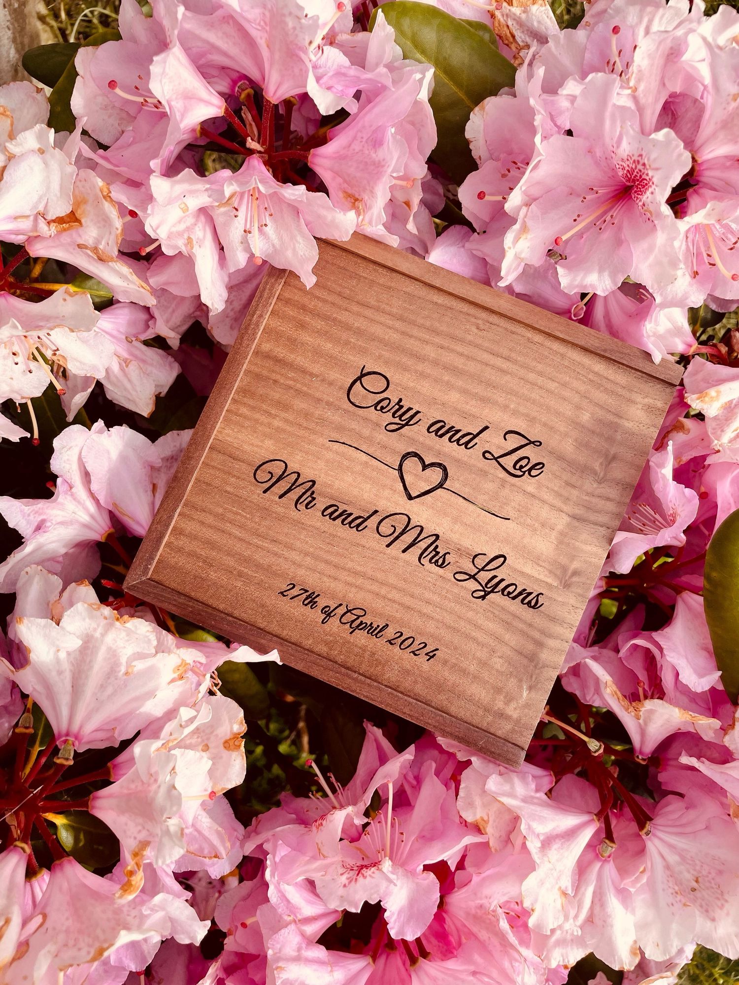 Wooden wedding keepsake box surrounded by pink azalea blossoms with engraved names and date.