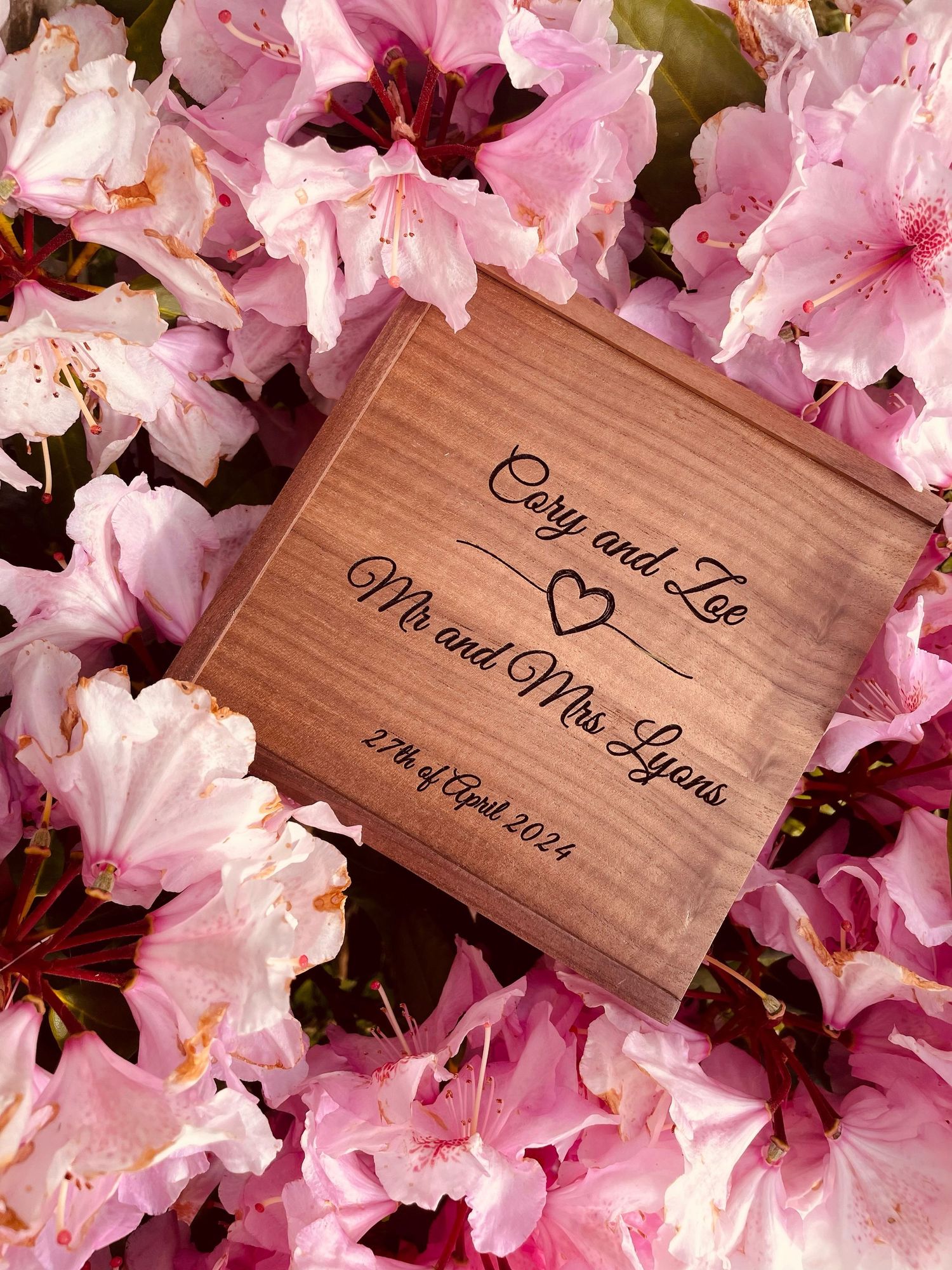 Personalized wooden wedding box with heart detail photographed among vibrant pink azaleas.