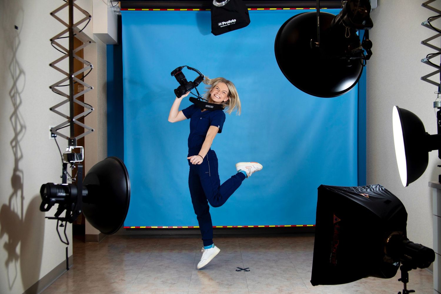 Women wearing scrubs jumping and smiling with a camera in hand in front of a studio set-up.