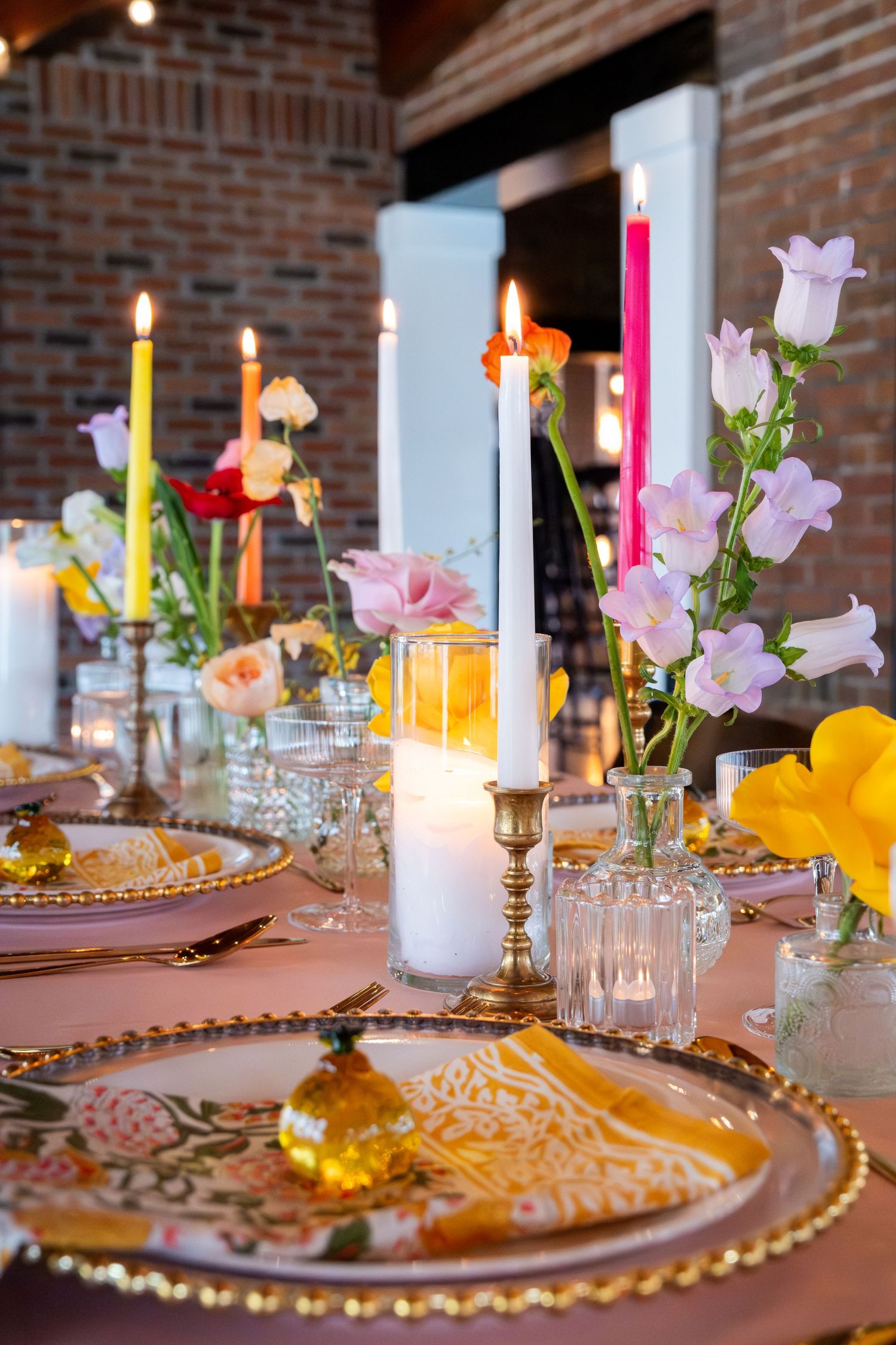 Elegant wedding reception table with colorful taper candles, spring flowers, and gold-rimmed charger plates.