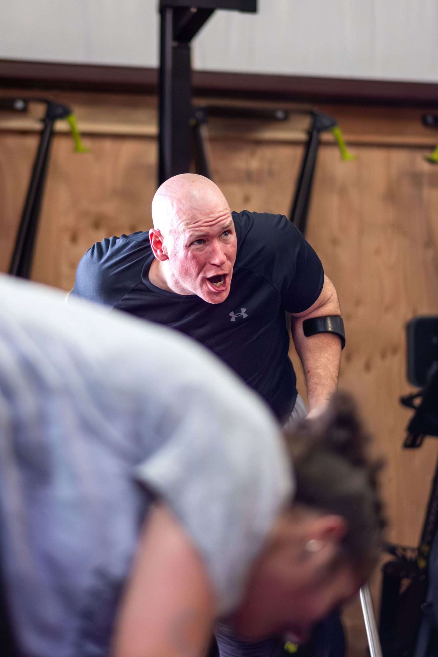 Bald male coach intensely motivates an athlete during a CrossFit workout in a gym.