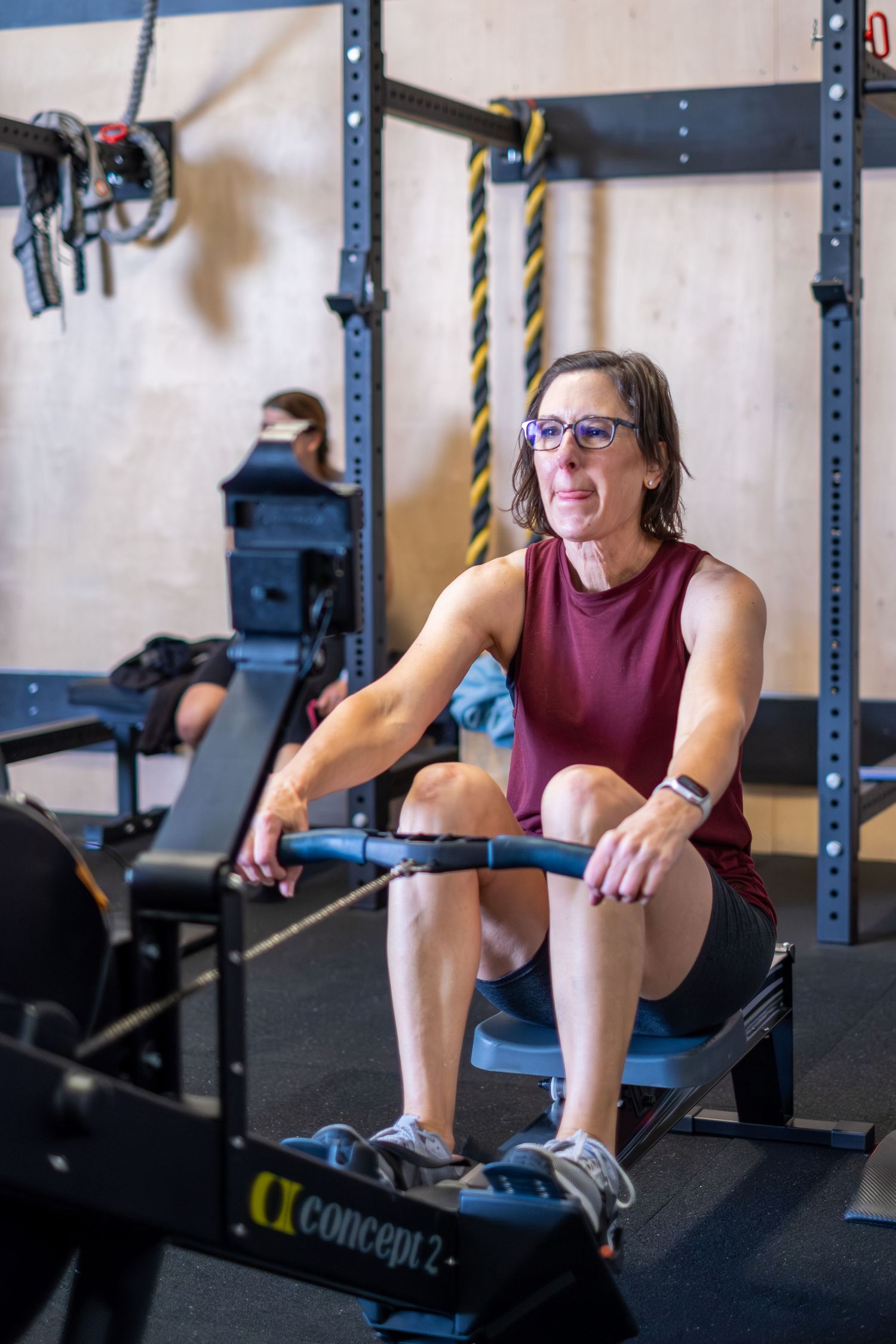 Woman wearing glasses using a Concept2 rowing machine during a gym workout.